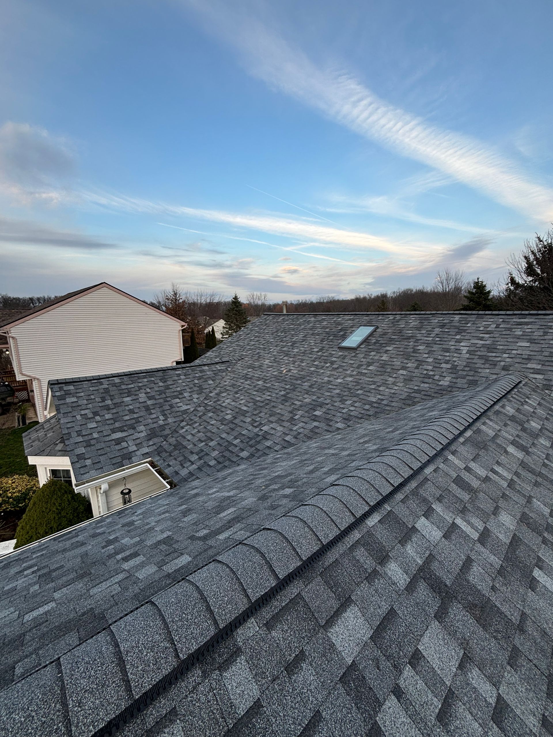 Two roofers kneeling on a roof, one hammering shingles.