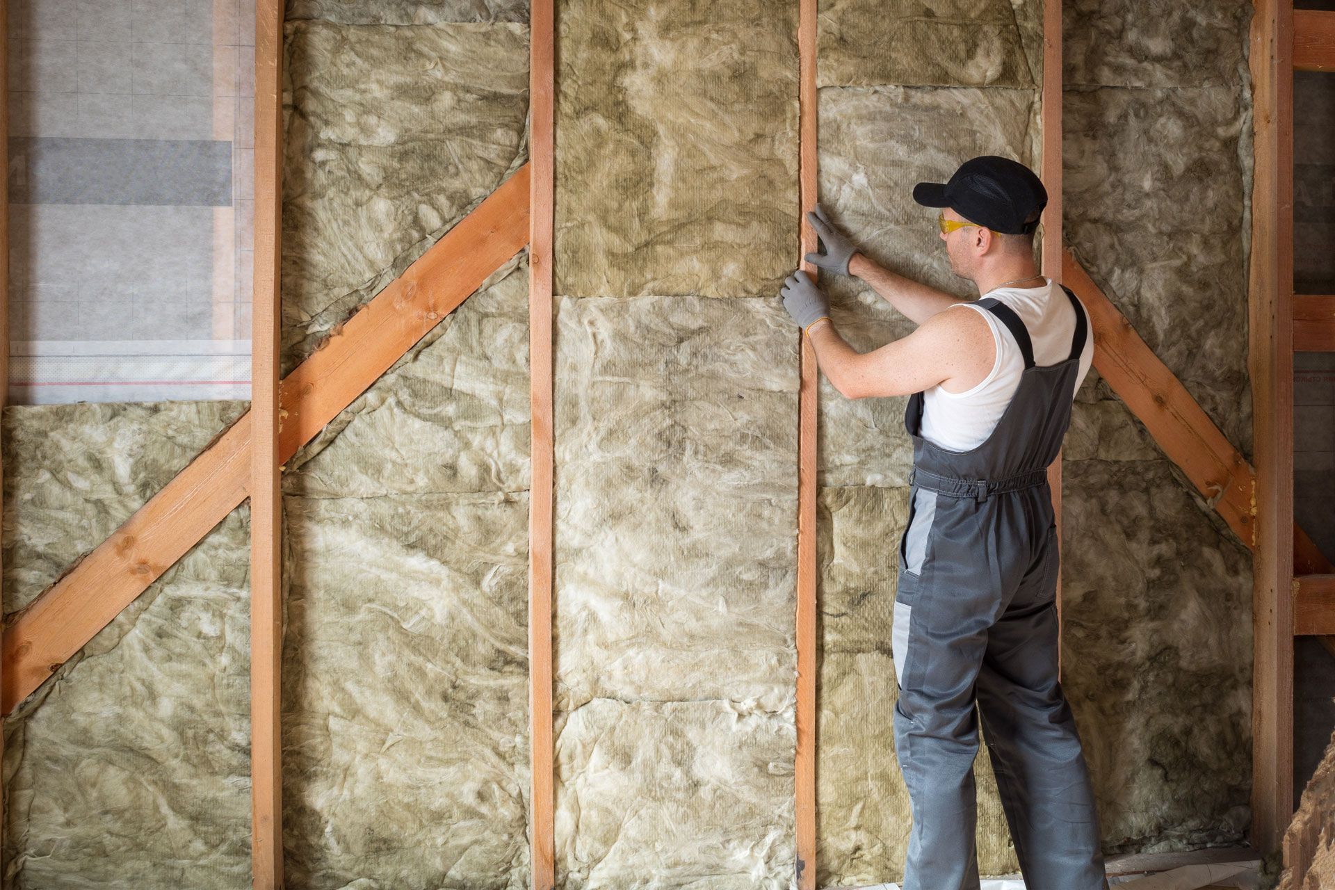Man installing insulation between wooden studs in a wall.