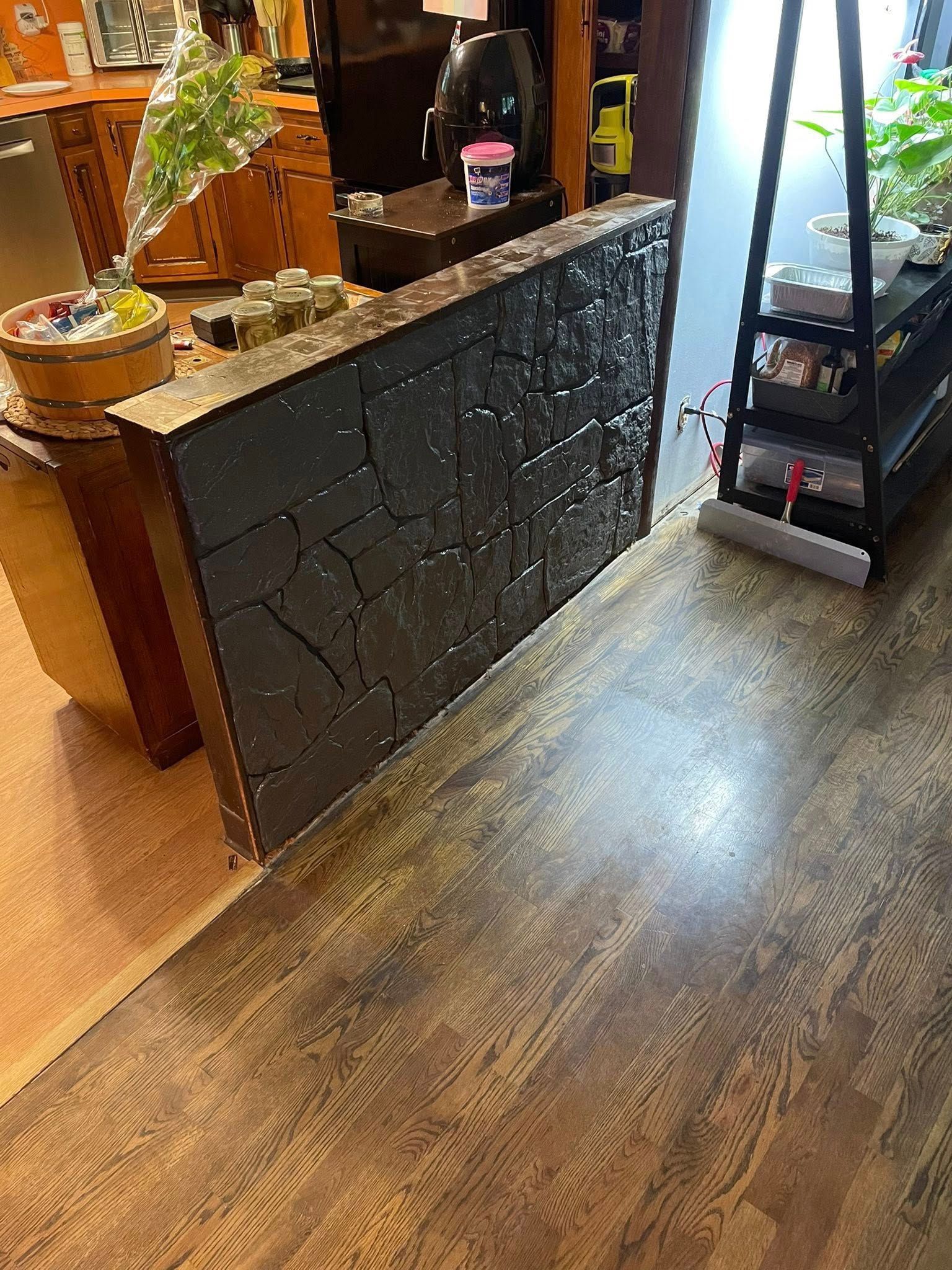 Dark, textured wall panel leaning against a countertop, set in a room with hardwood floors and other objects.