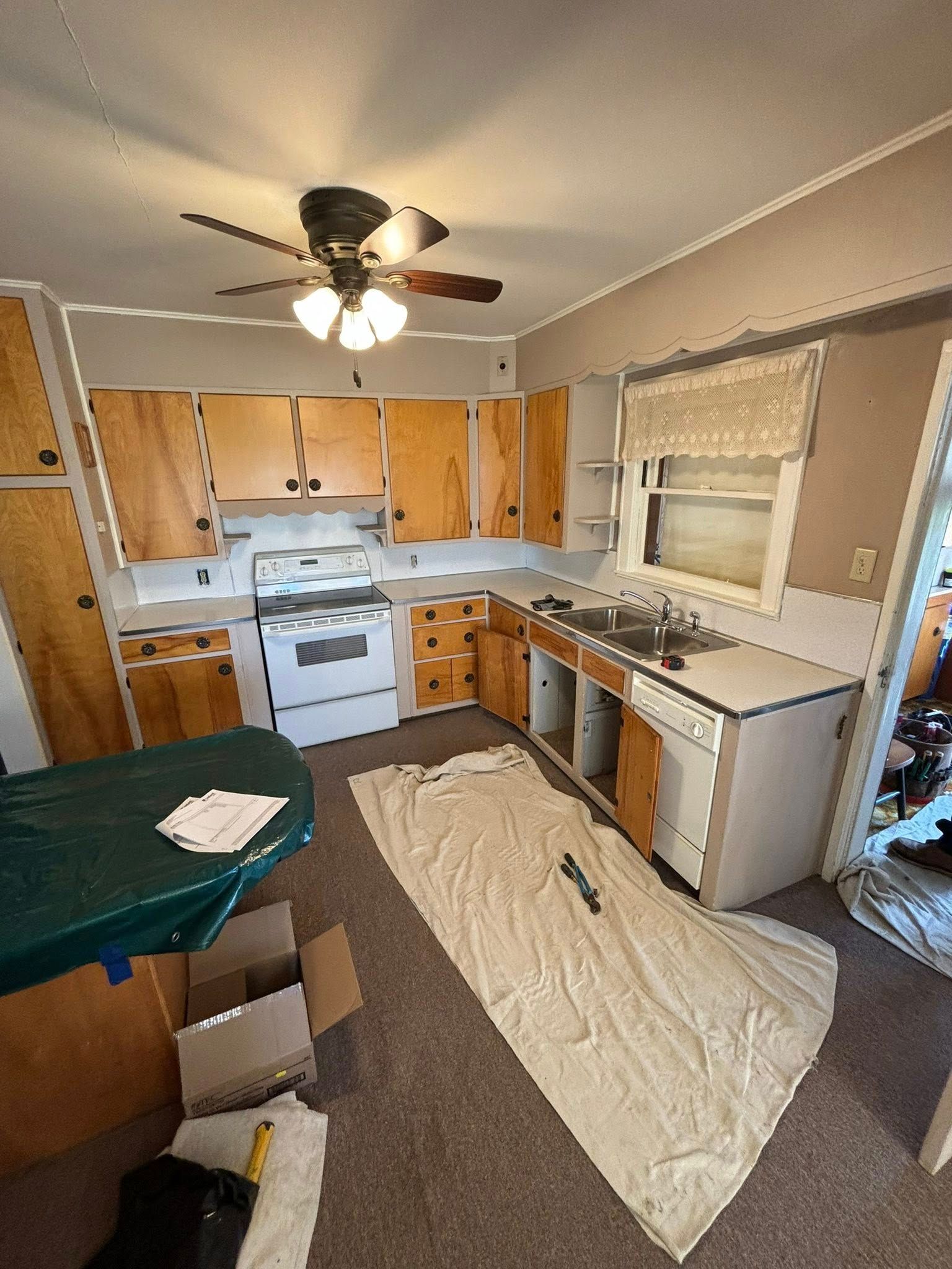 Kitchen with wooden cabinets and white appliances undergoing renovation. A drop cloth covers the floor.