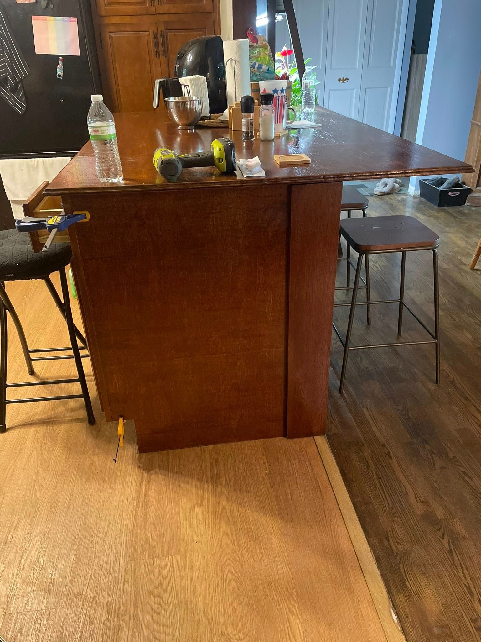 A kitchen island with stools, rug, and items on the countertop. Wooden cabinet and floor.