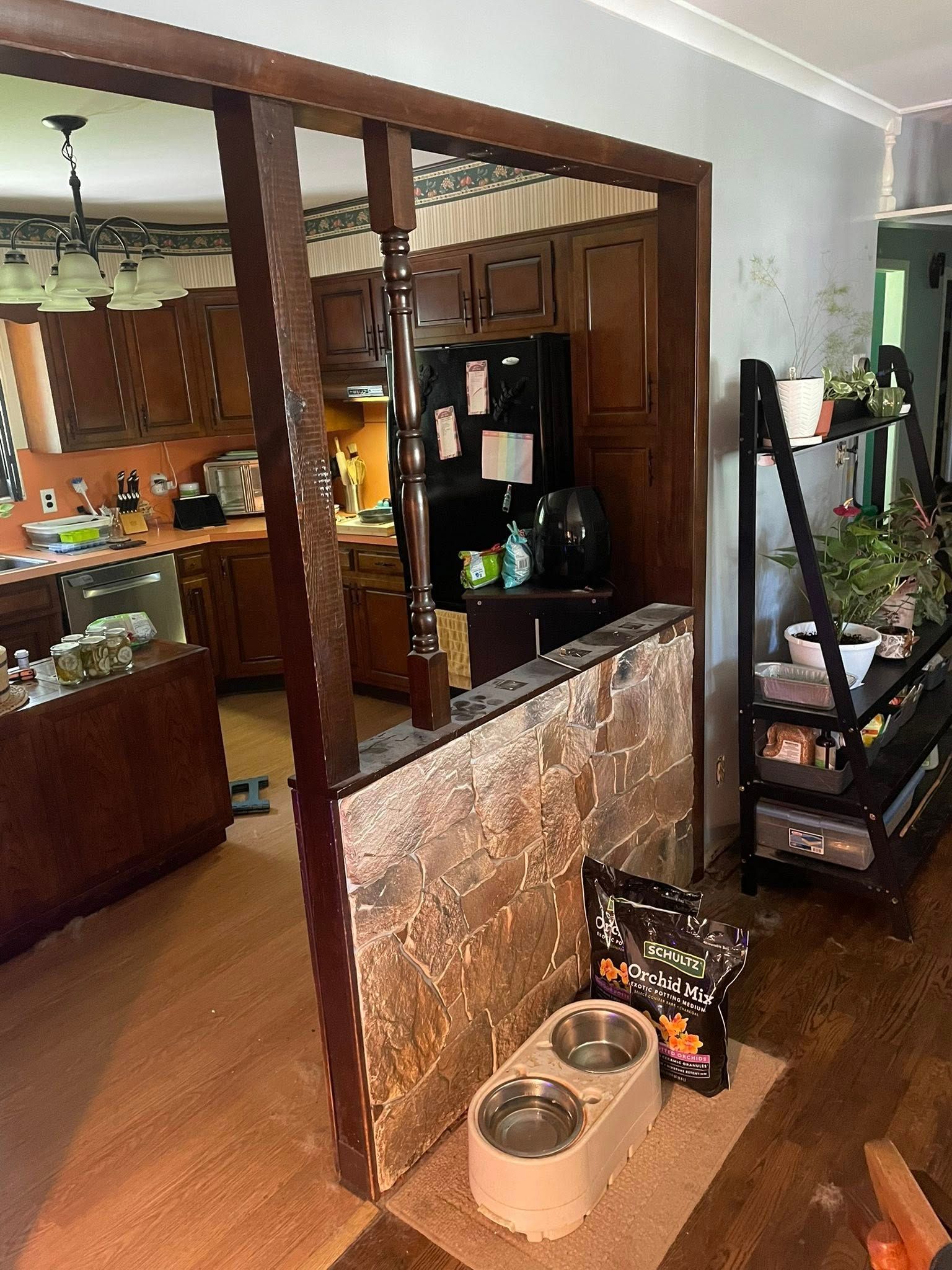 Interior view of kitchen and living area, partial wall with wood posts, dog bowls on floor.