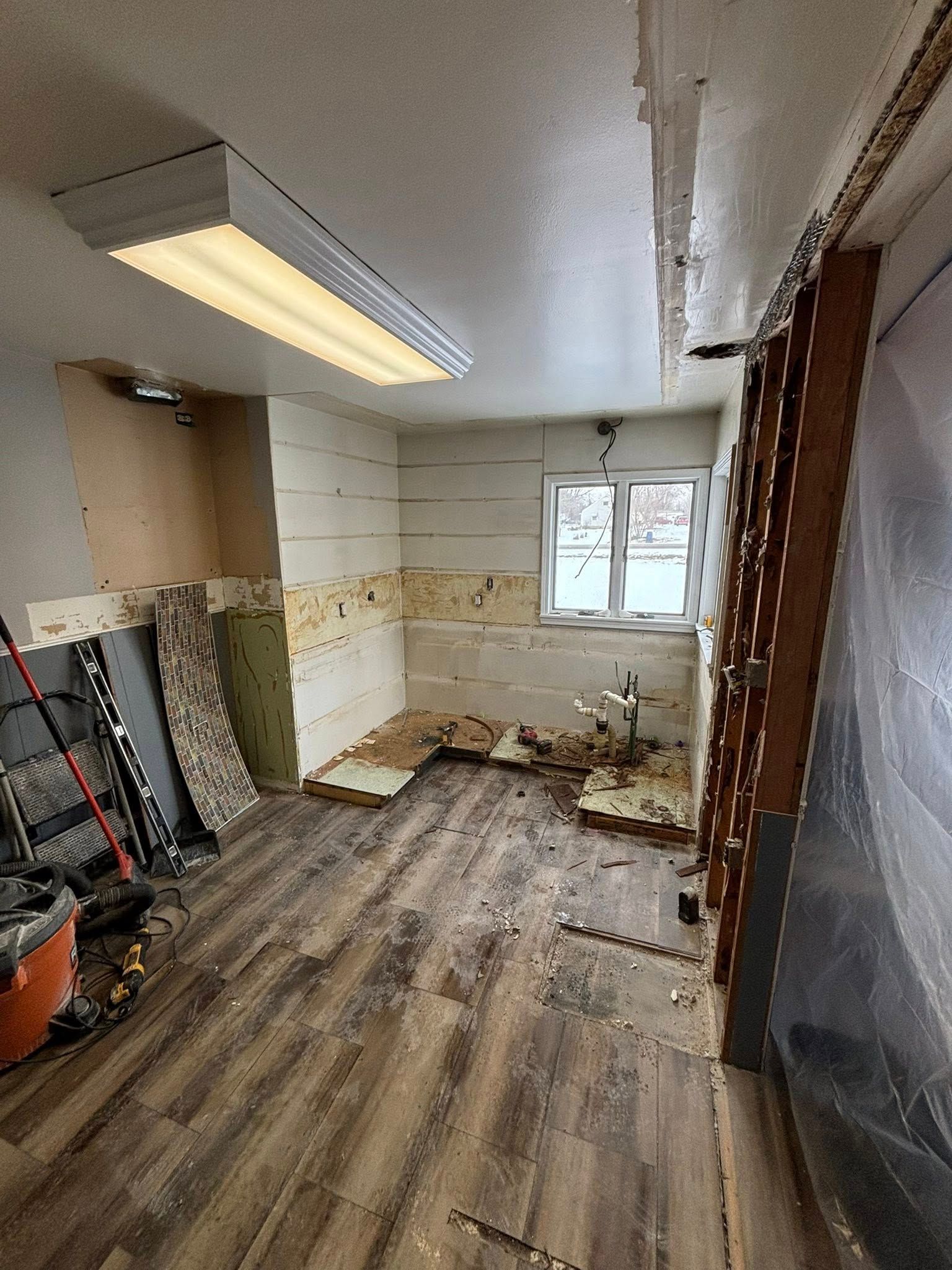 Interior room under renovation; exposed walls, damaged floor, work tools visible, and a window.