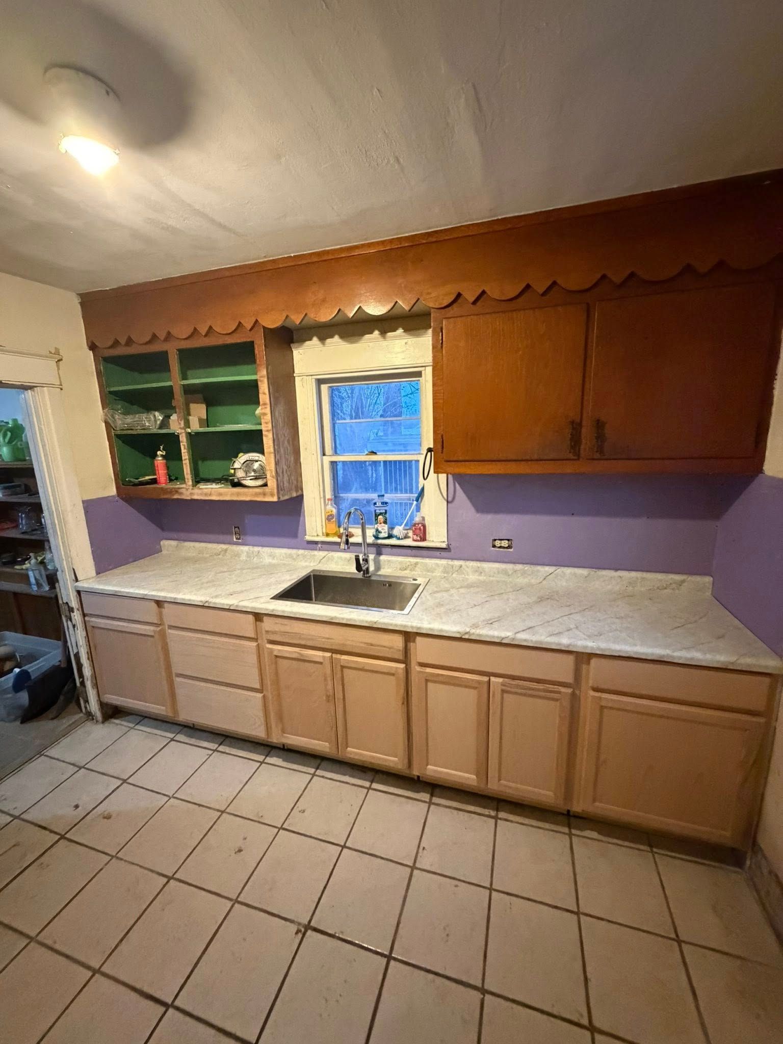 Kitchen with light-colored cabinets, countertop, purple wall, window, and sink.