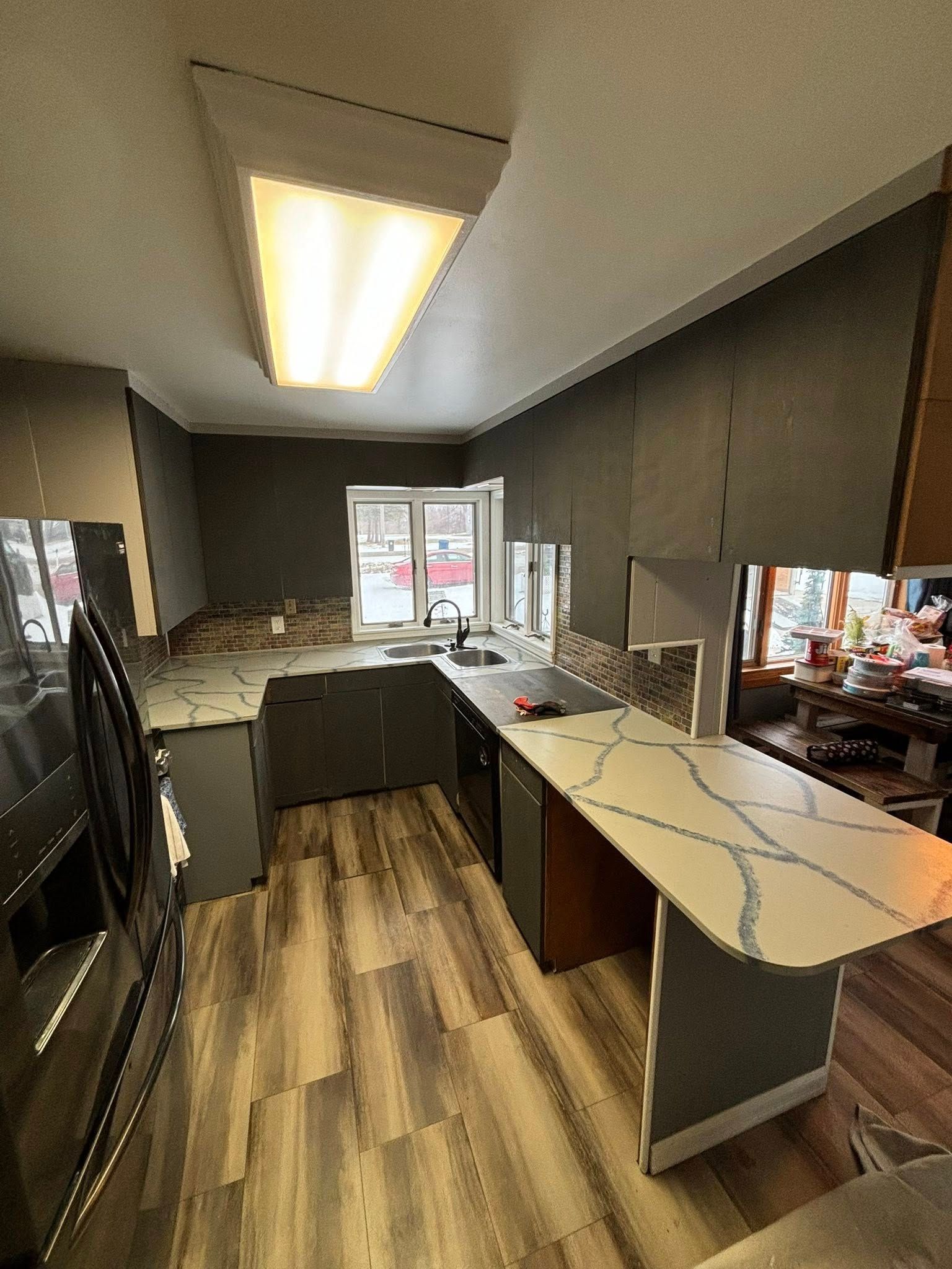 Modern kitchen with gray cabinets, patterned countertops, wood flooring, and a window.