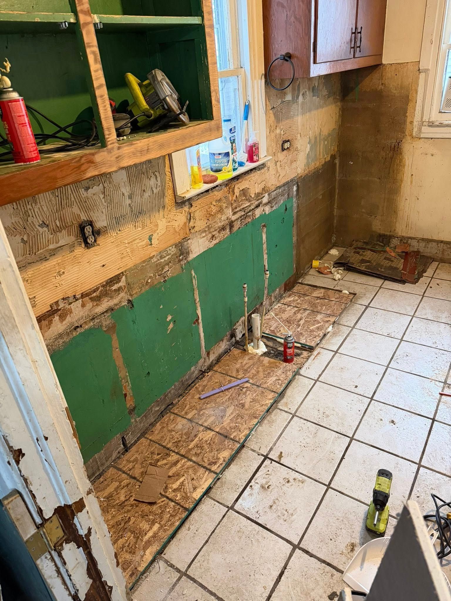 Kitchen undergoing renovation; exposed wall studs, green backing, and tile floor visible. Cabinets and tools present.