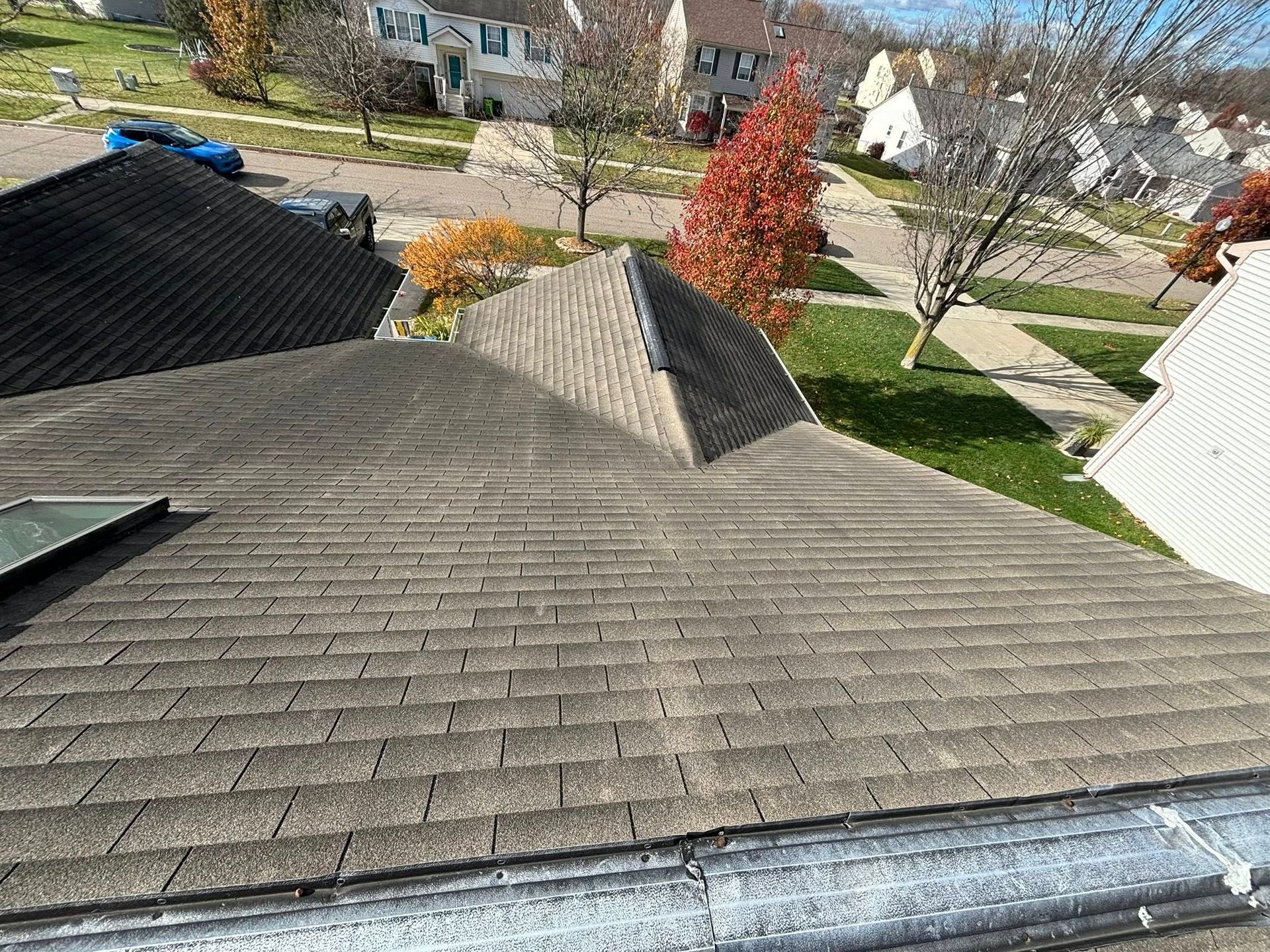 Brown shingle roof with a vent, overlooking a suburban neighborhood on a sunny day.