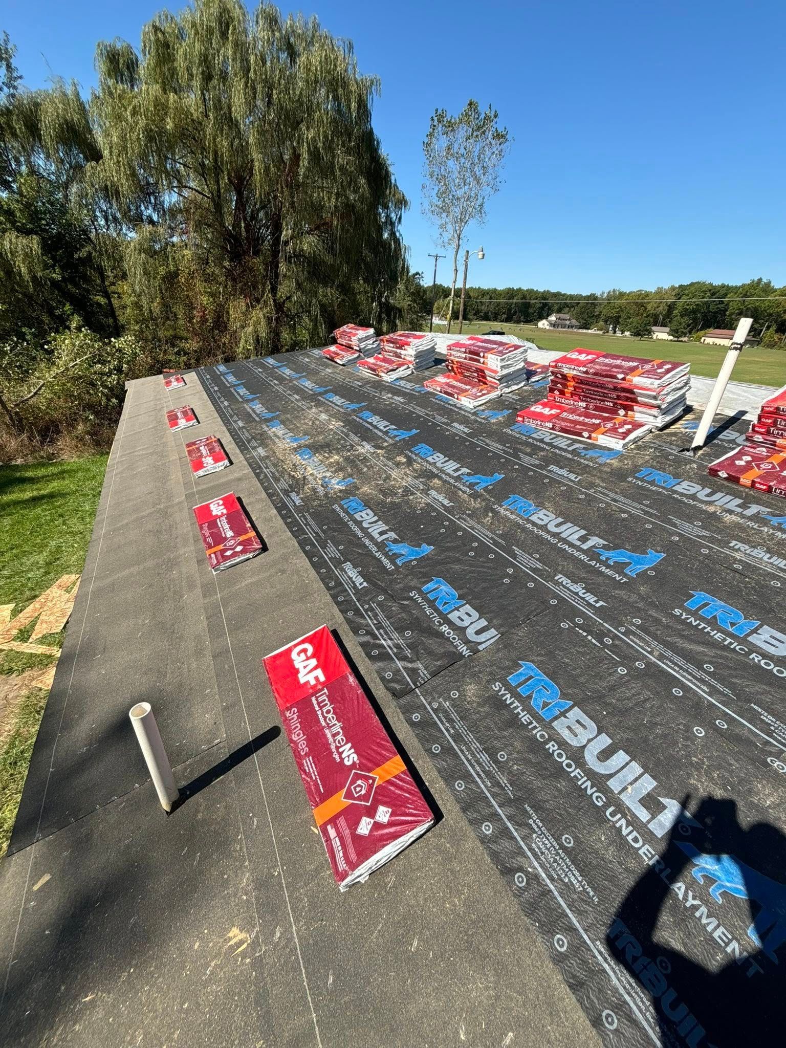 Roof under construction with shingles and materials laid out under a blue sky.