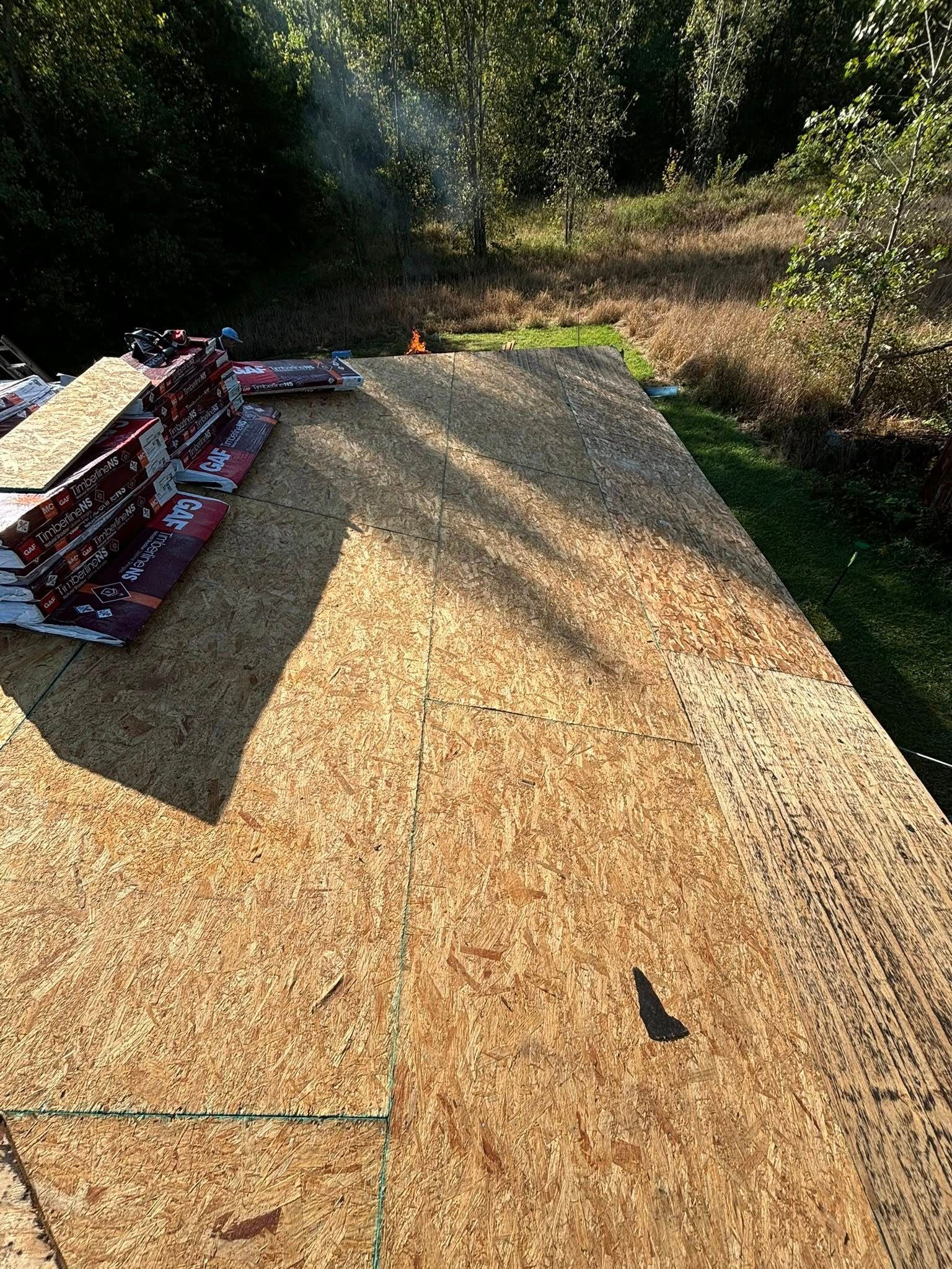 Rooftop with OSB sheathing partially covered with shingles. Several bundles of shingles sit on the left.