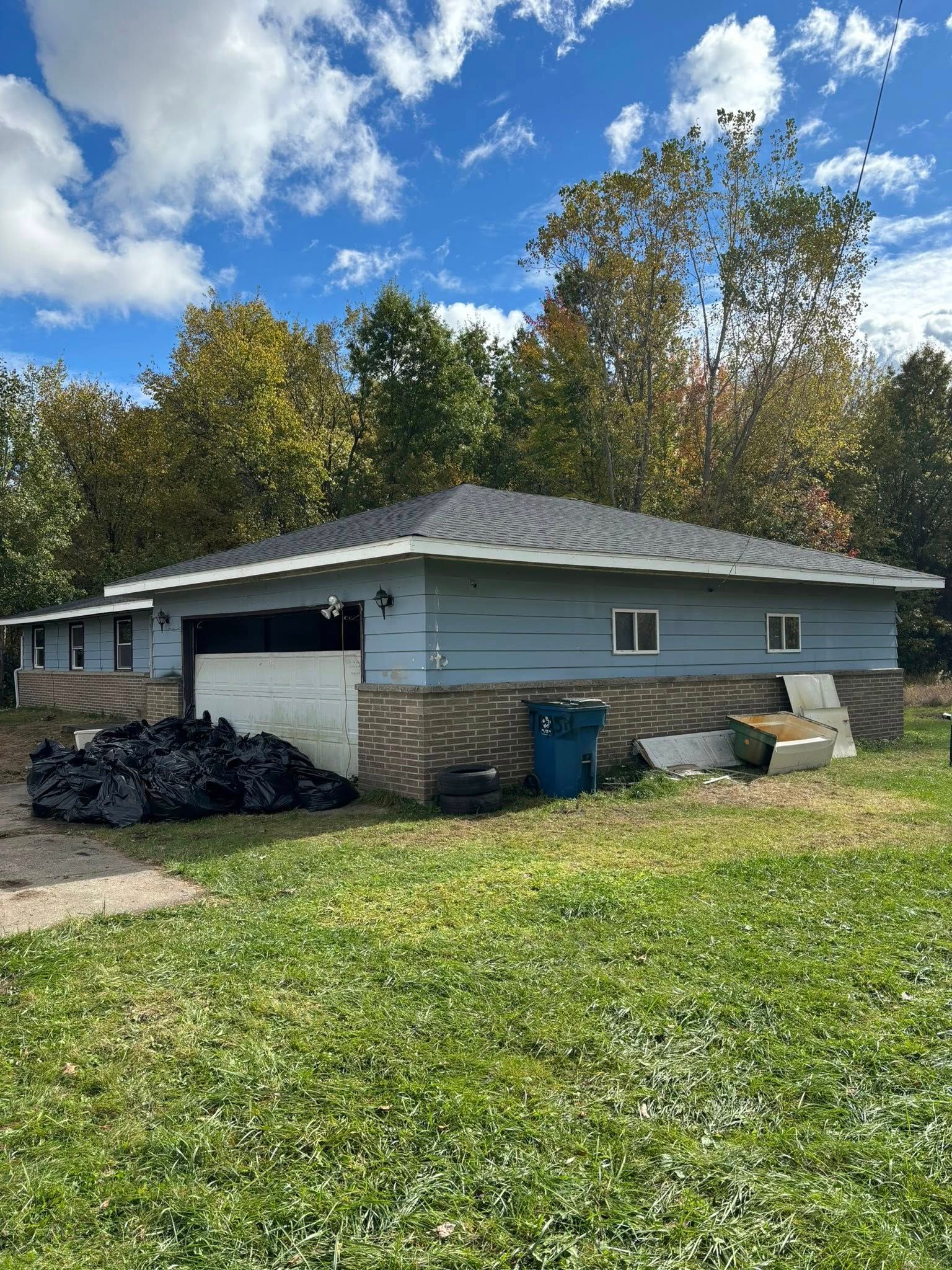 House under construction with blue siding, brown brick base, dark roof, and debris in the yard.