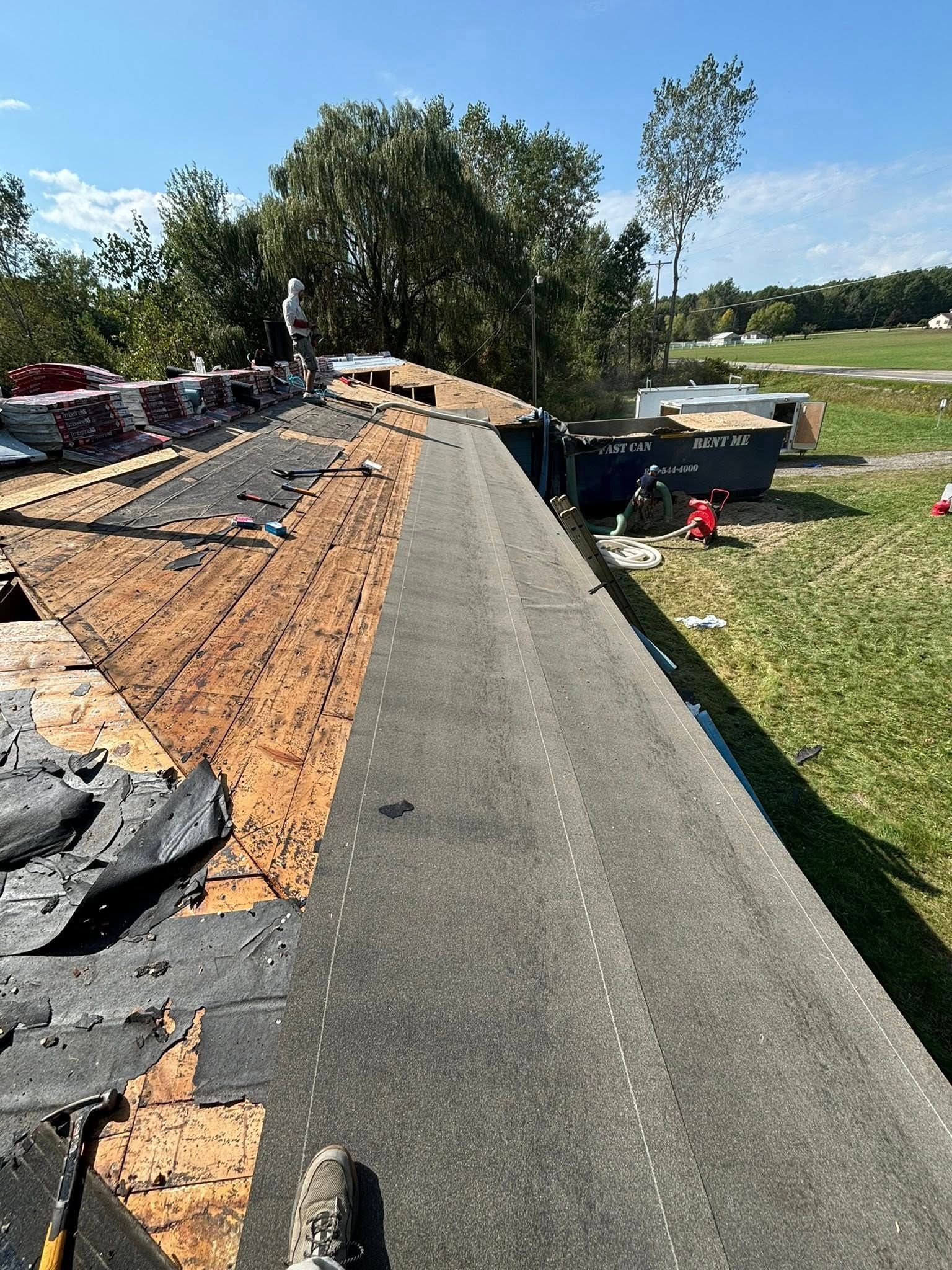 Roof being repaired; worker on the roof applying asphalt shingles, some old shingles and wood decking are visible.