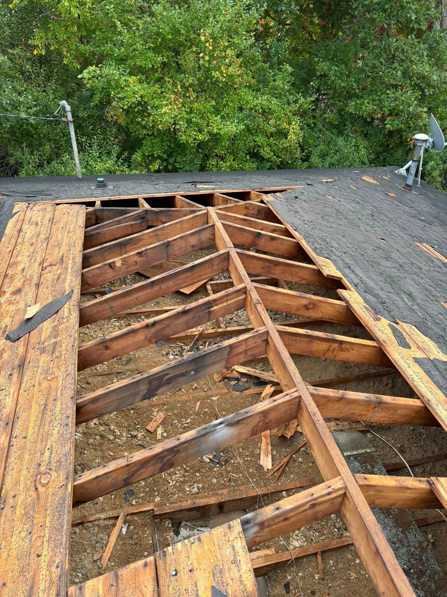 Roof with missing shingles and exposed wooden framework. Green trees in background.
