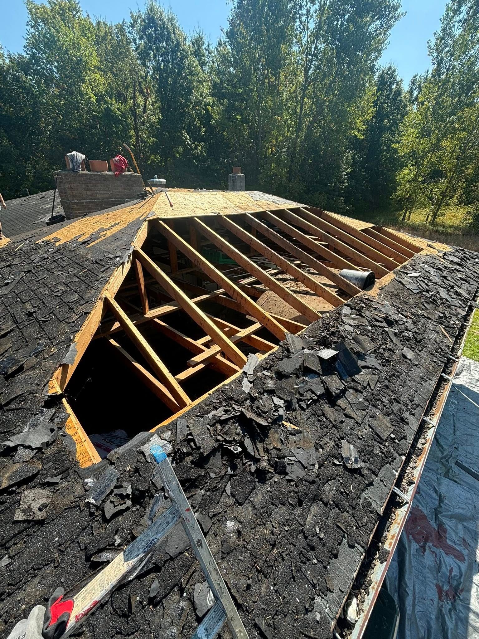 Roof being repaired, showing exposed wooden rafters and partially removed asphalt shingles.