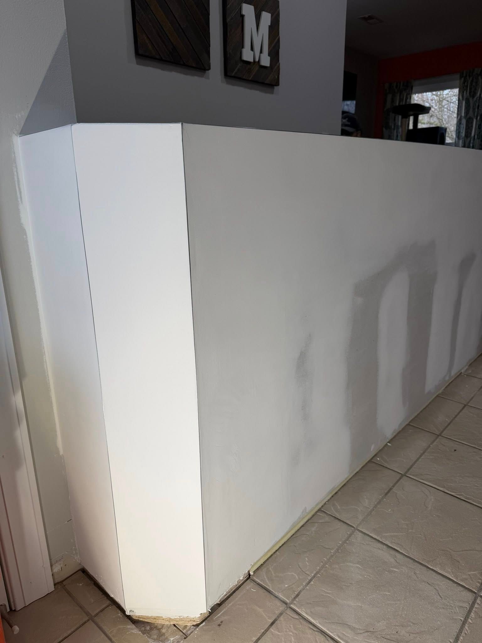 White drywall half-wall with corner, partially primed, against a tiled floor and a doorway.
