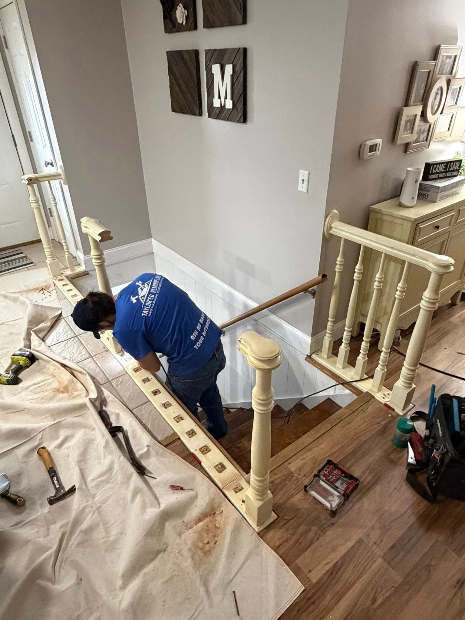 Person installing a staircase banister indoors. Beige and white elements in a home setting.