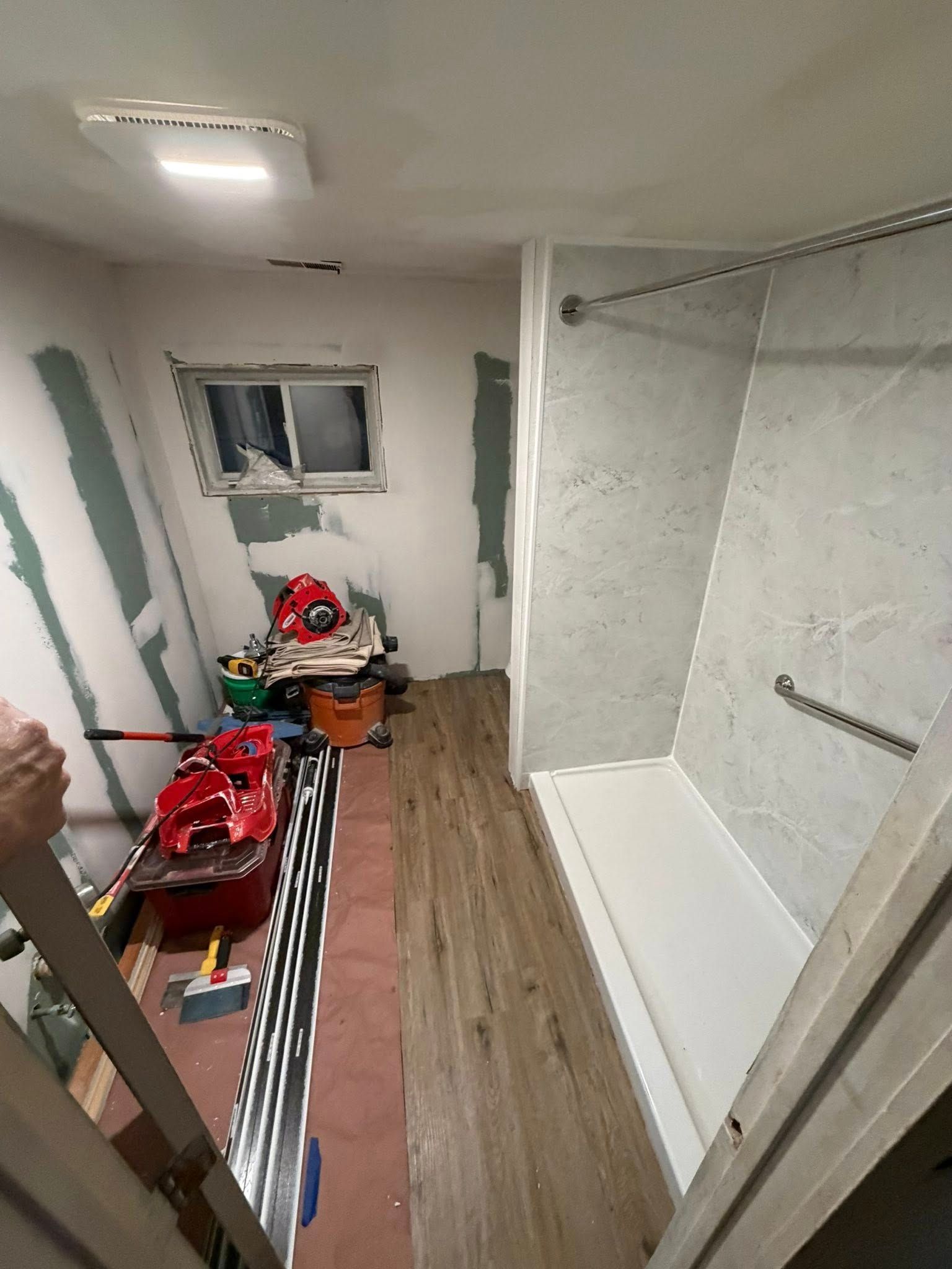 Bathroom under renovation, with shower stall, window, tools, and exposed wallboard.