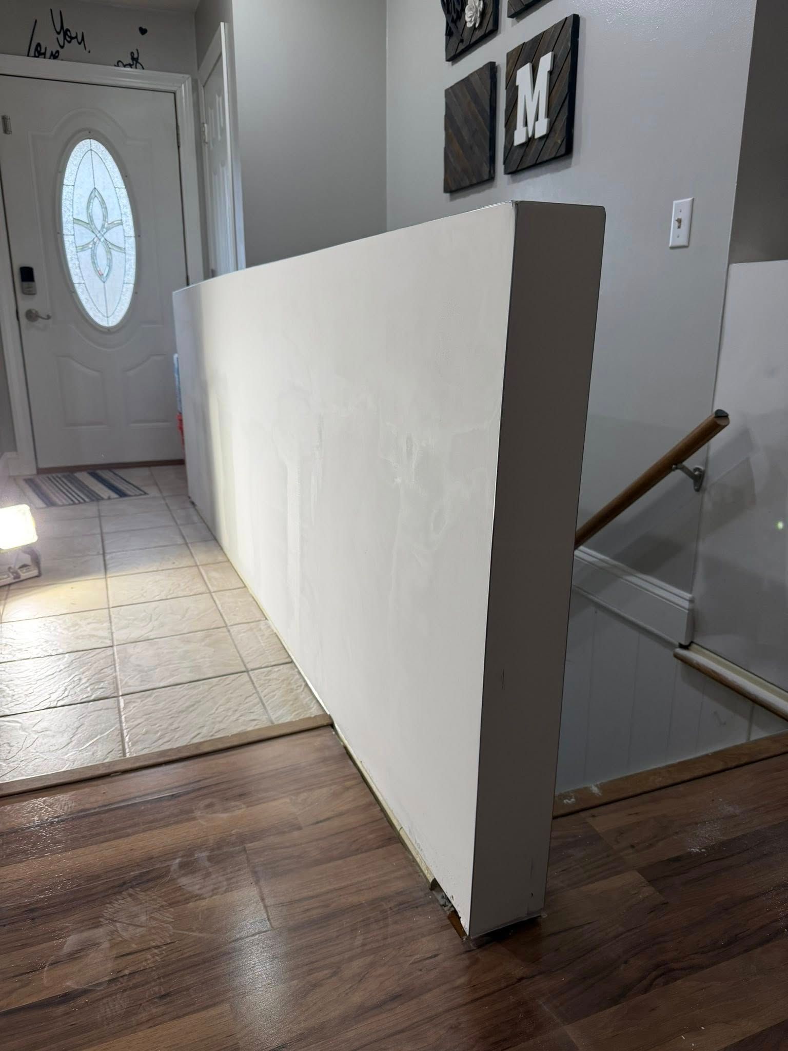 White wall partially blocking a doorway, light wood floor, and steps.