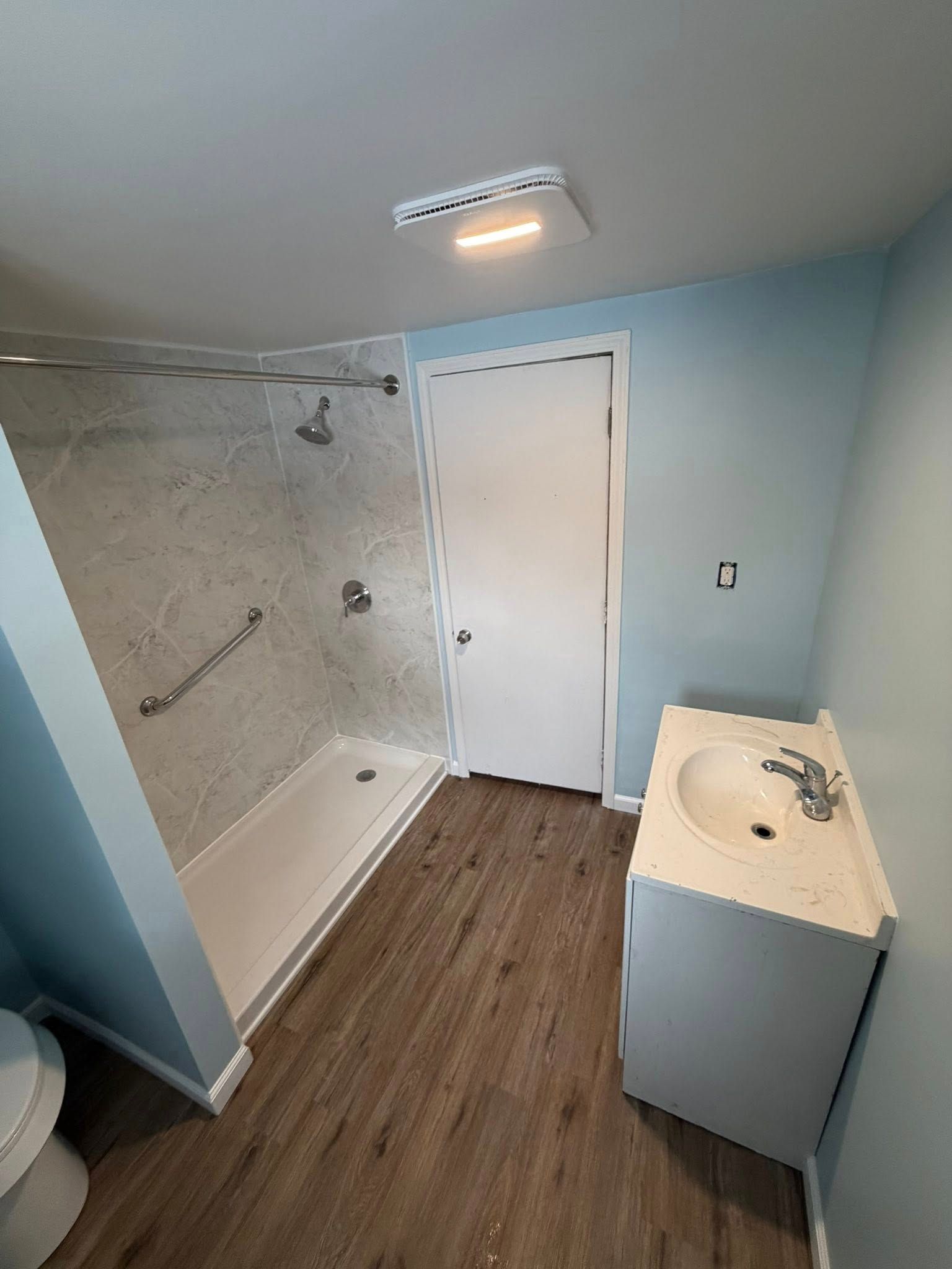 Bathroom with a shower, vanity, and toilet; blue walls, wood-look floor.