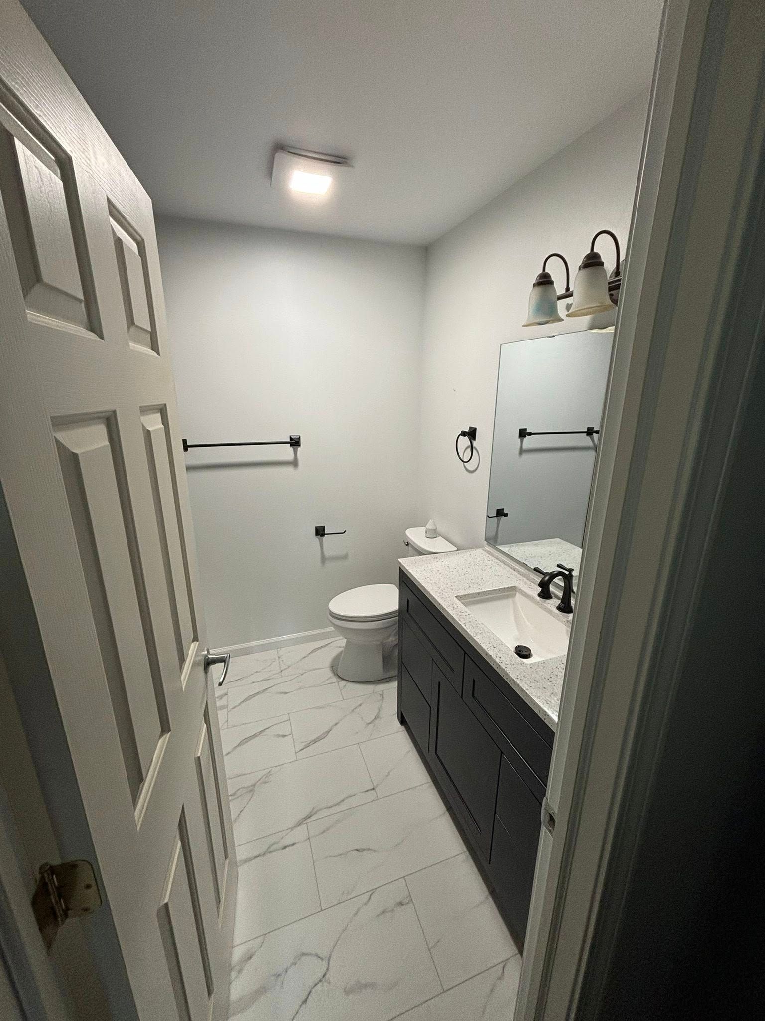 Bathroom interior, white walls, dark vanity, black hardware, white tile floor.