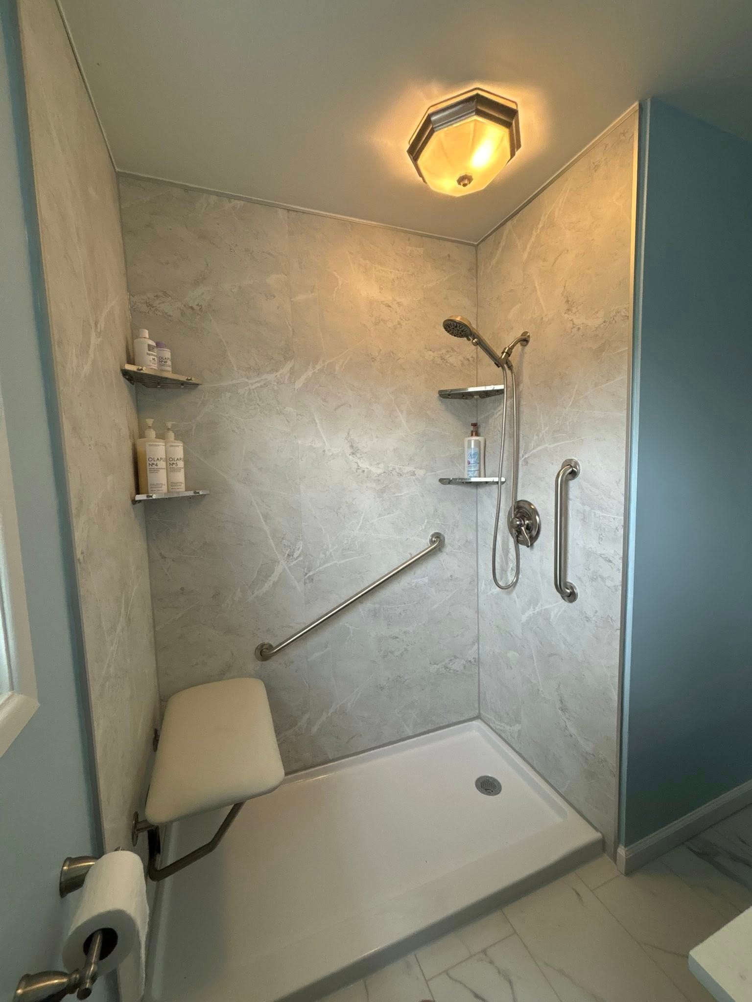Accessible shower with grab bars, shower seat, and stone-like walls.