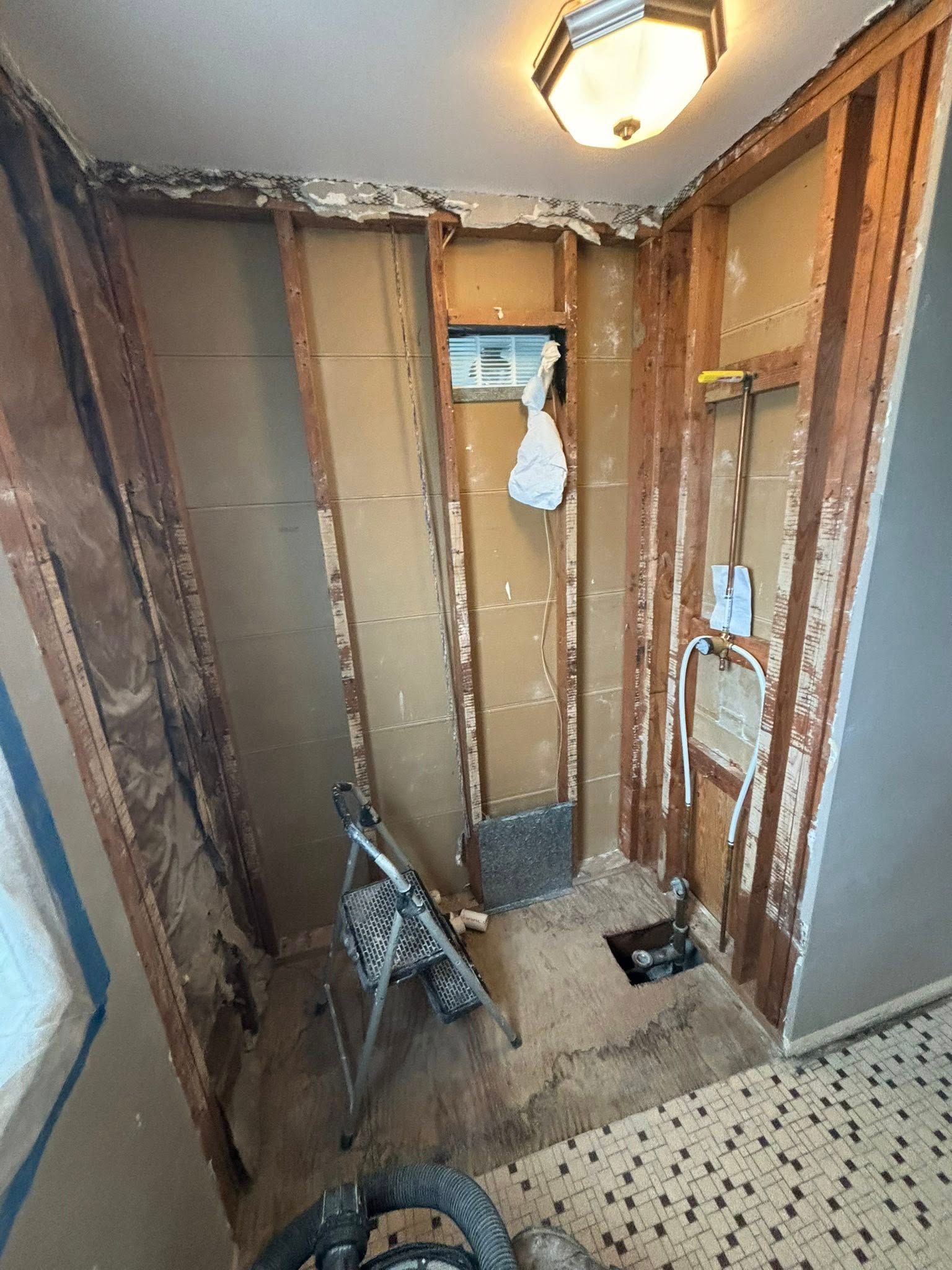 Bathroom renovation in progress, walls stripped to studs. Visible plumbing, electrical work, and debris on the floor.