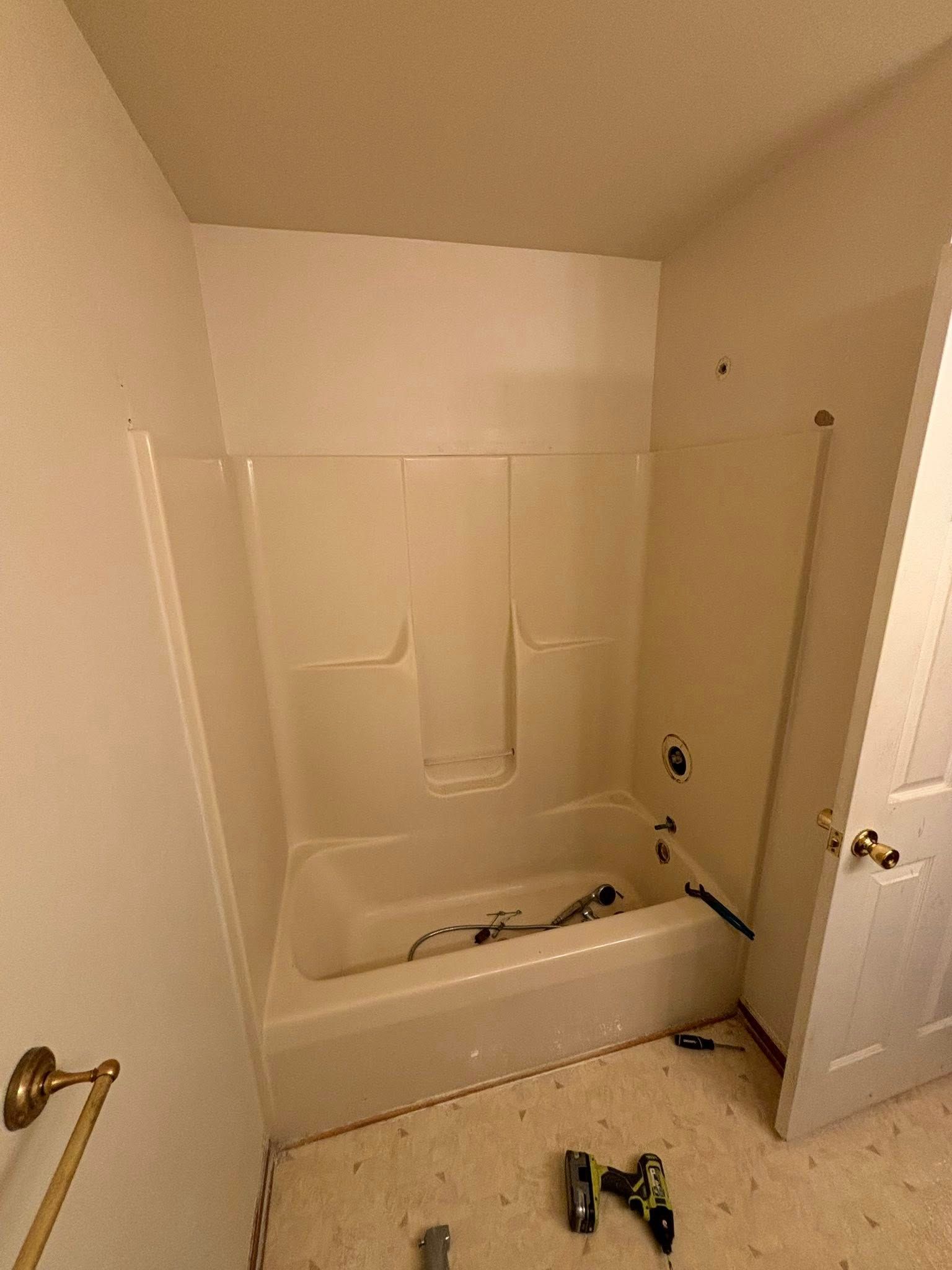 Bathroom with a white bathtub and surrounding walls, door is open, construction tools on floor.