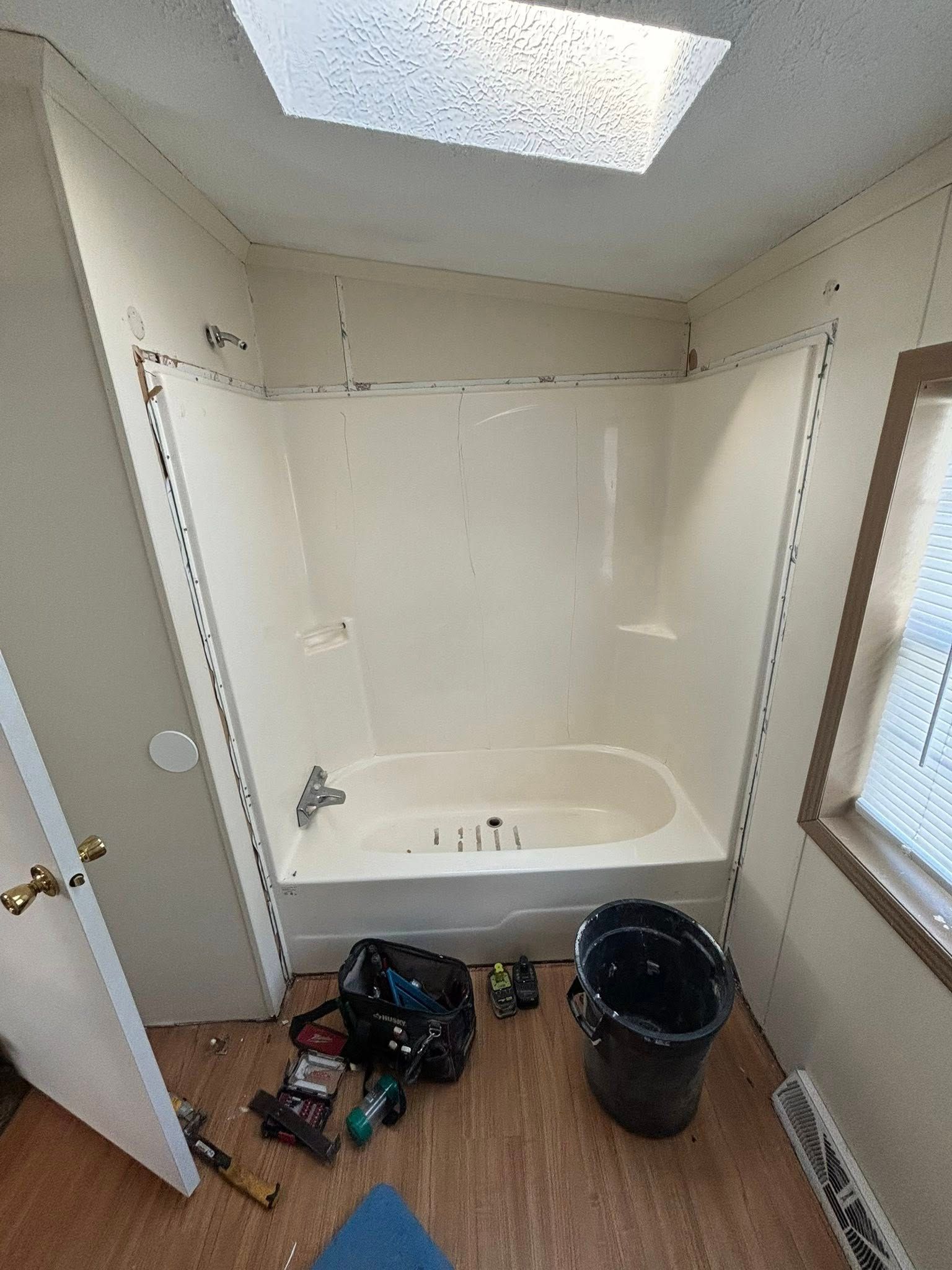 Bathroom under renovation; white shower and walls, brown floor, skylight. Tools and trash bags on floor.