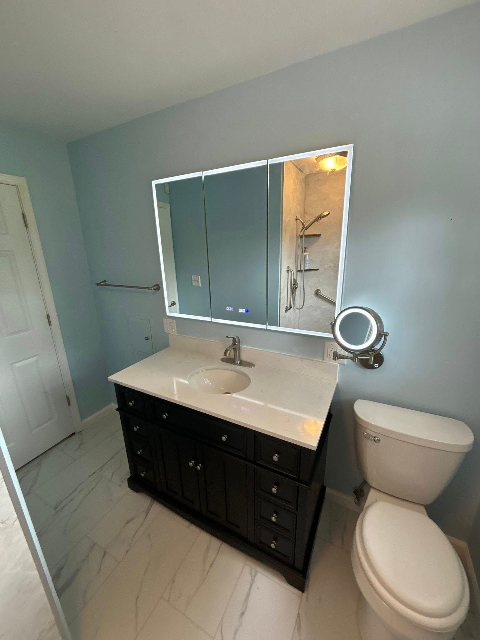 Bathroom with dark vanity, white countertop, and light blue walls. A large mirror hangs over the sink.