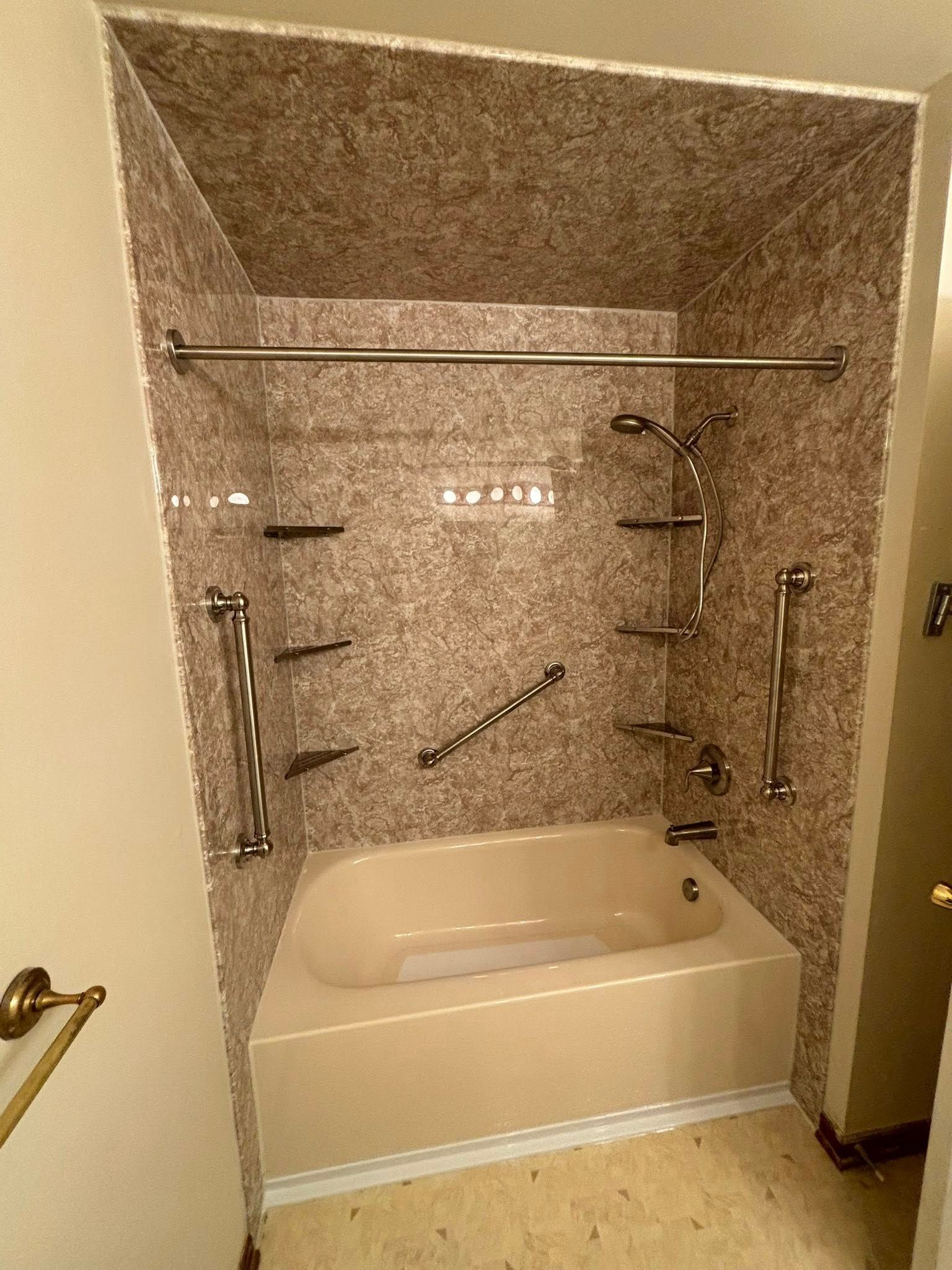 Shower/tub combo with safety bars, shelves, and grab bars. Beige tub with speckled brown walls and chrome fixtures.