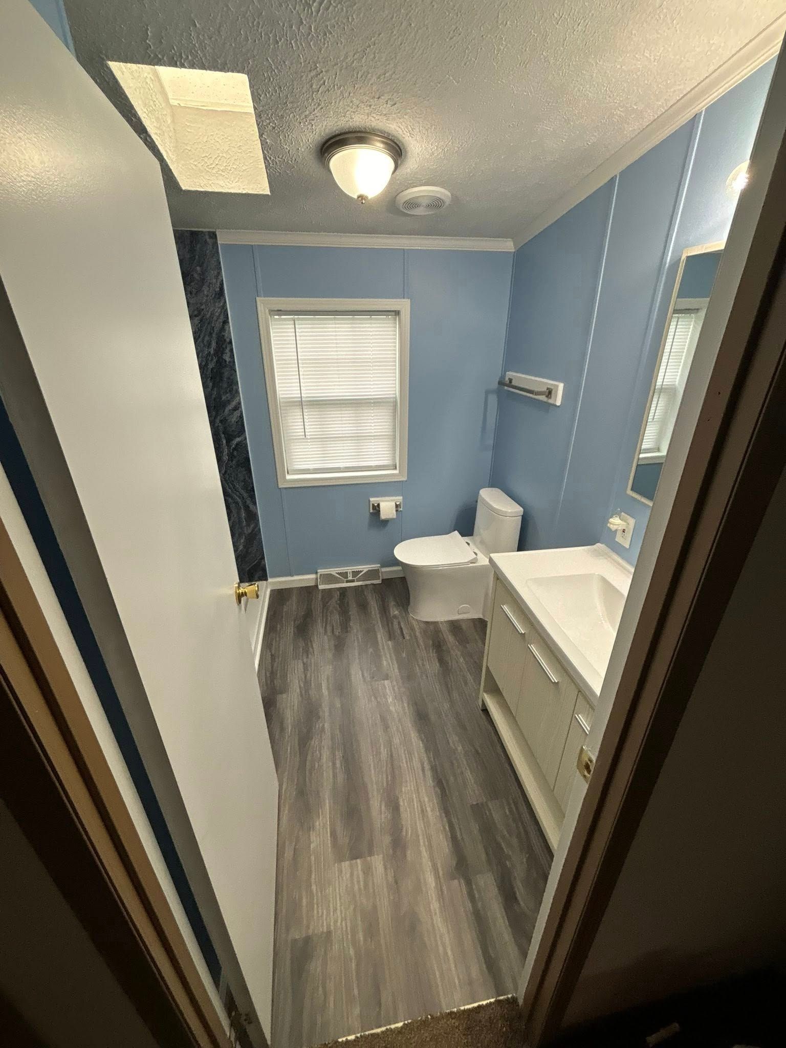 Bathroom with blue walls, white fixtures, and gray flooring. View from the doorway.