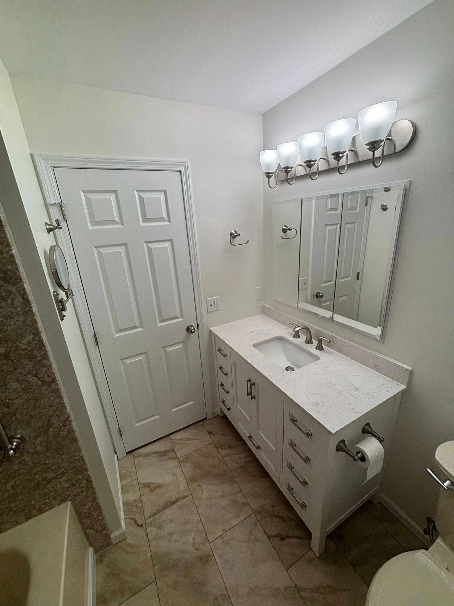 Bathroom with white vanity, mirror, lights, toilet, and a closed white door.