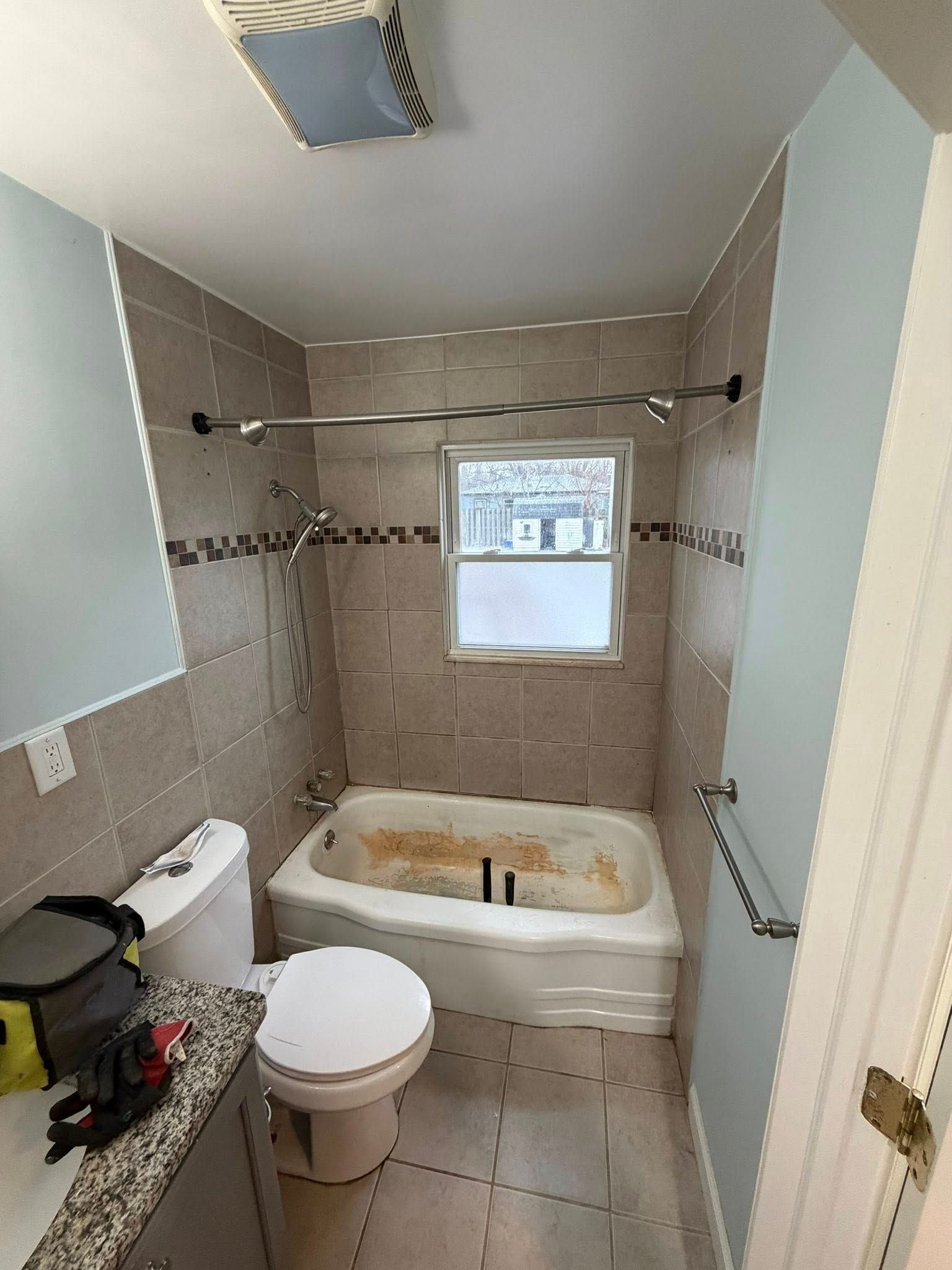 Bathroom with beige tile walls, a white bathtub, and a toilet. The room has a window.