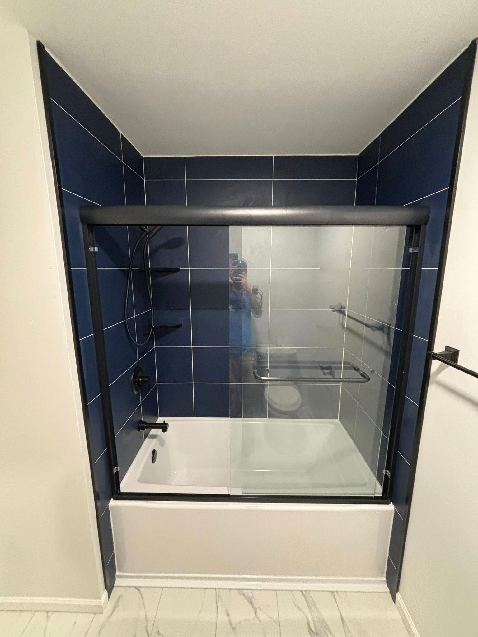 Blue-tiled shower with black-framed sliding glass door, white tub, and black fixtures.