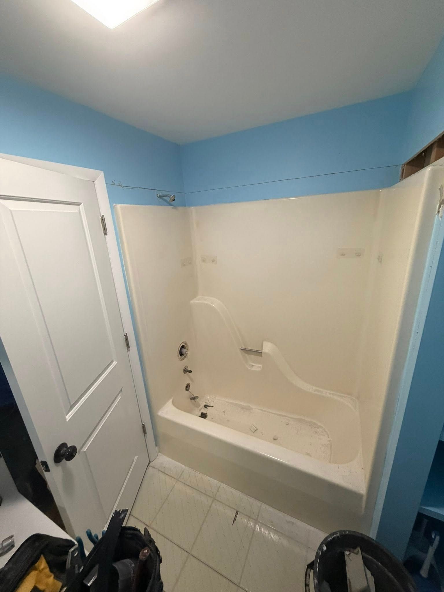 Bathroom interior with a white bathtub and shower surround, blue walls, and a white door.