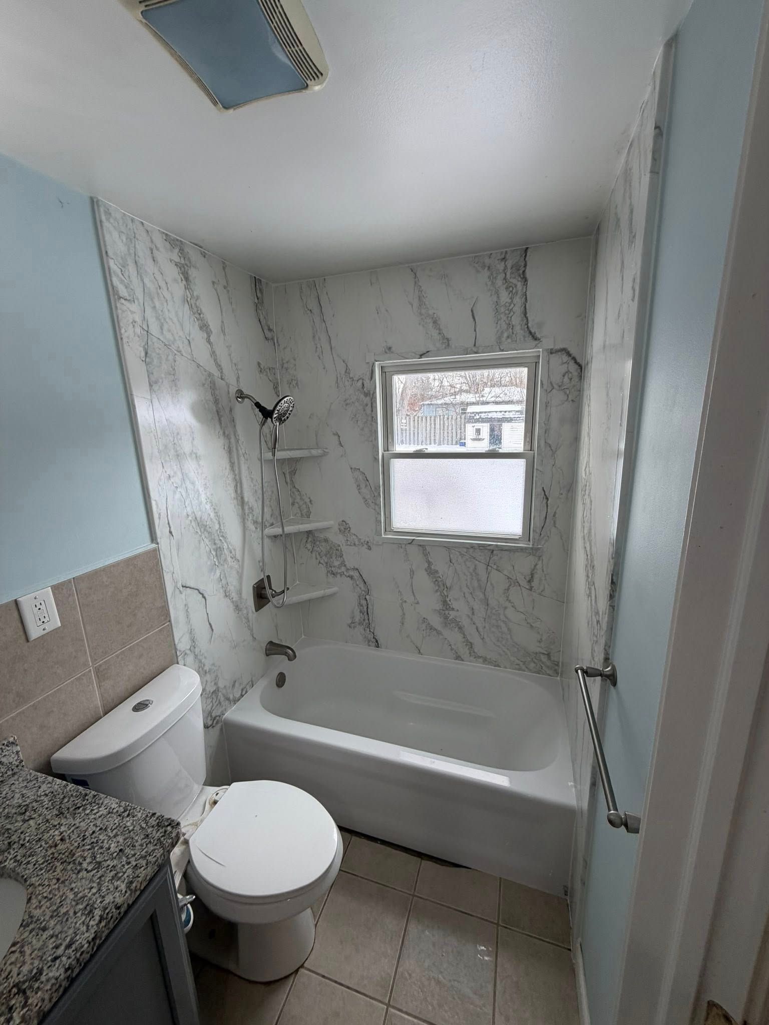Bathroom with tub, toilet, and marble-look wall. Includes window and shower fixture.
