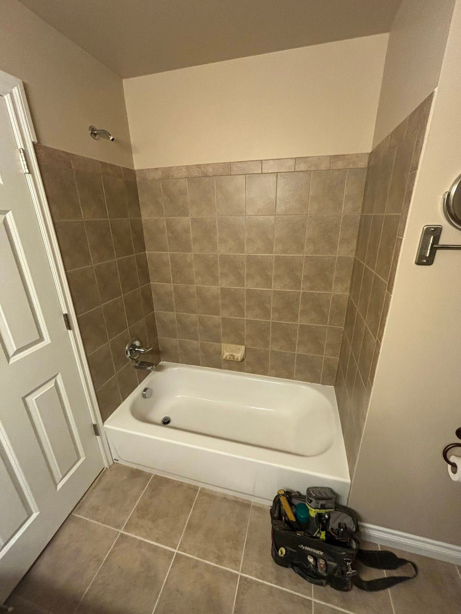 Bathroom with white tub, brown tile walls, and beige walls. Tool bag sits on the floor.