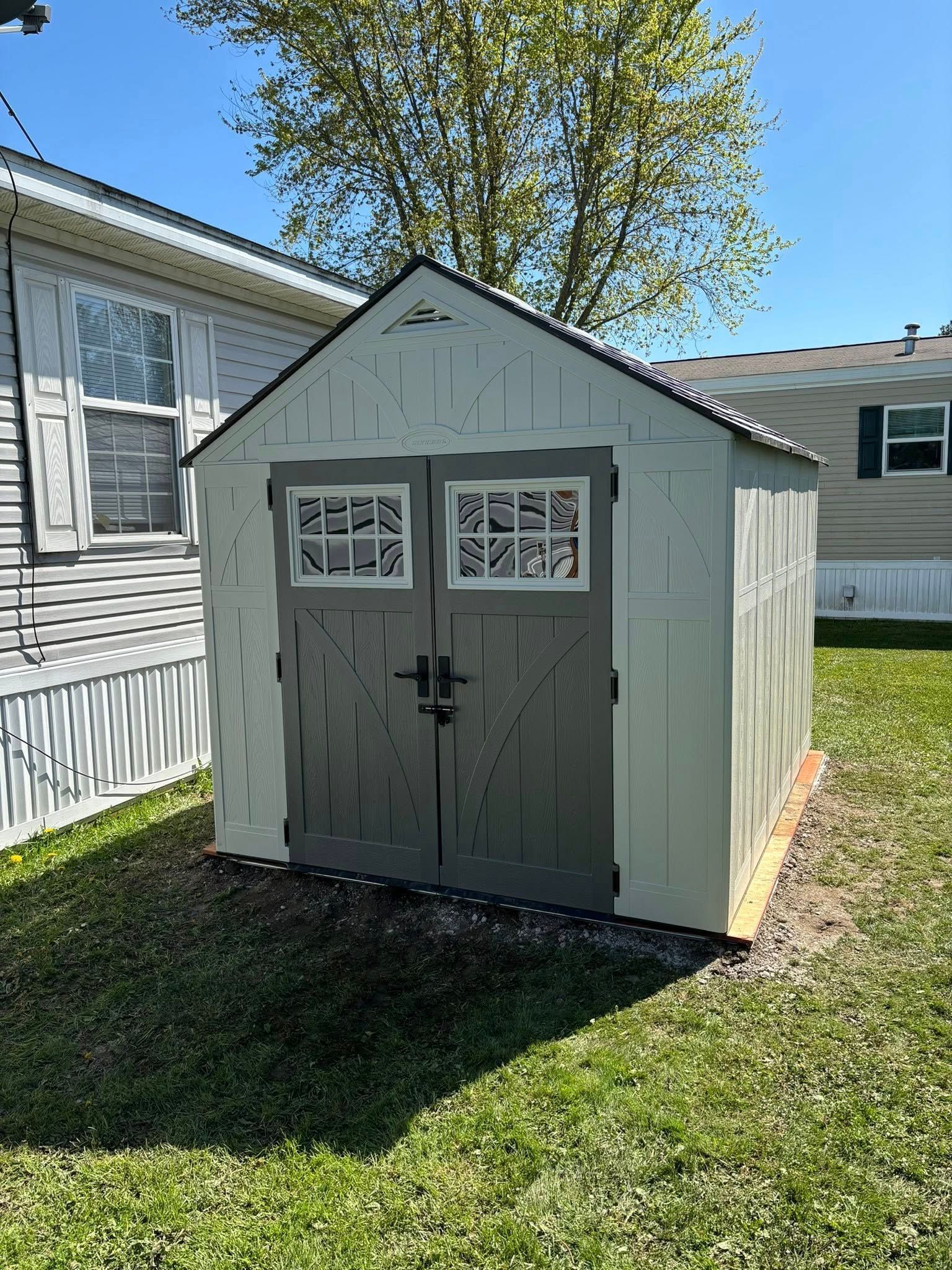 A light green shed with grey doors, a black roof, and white-framed windows, in a grassy backyard.