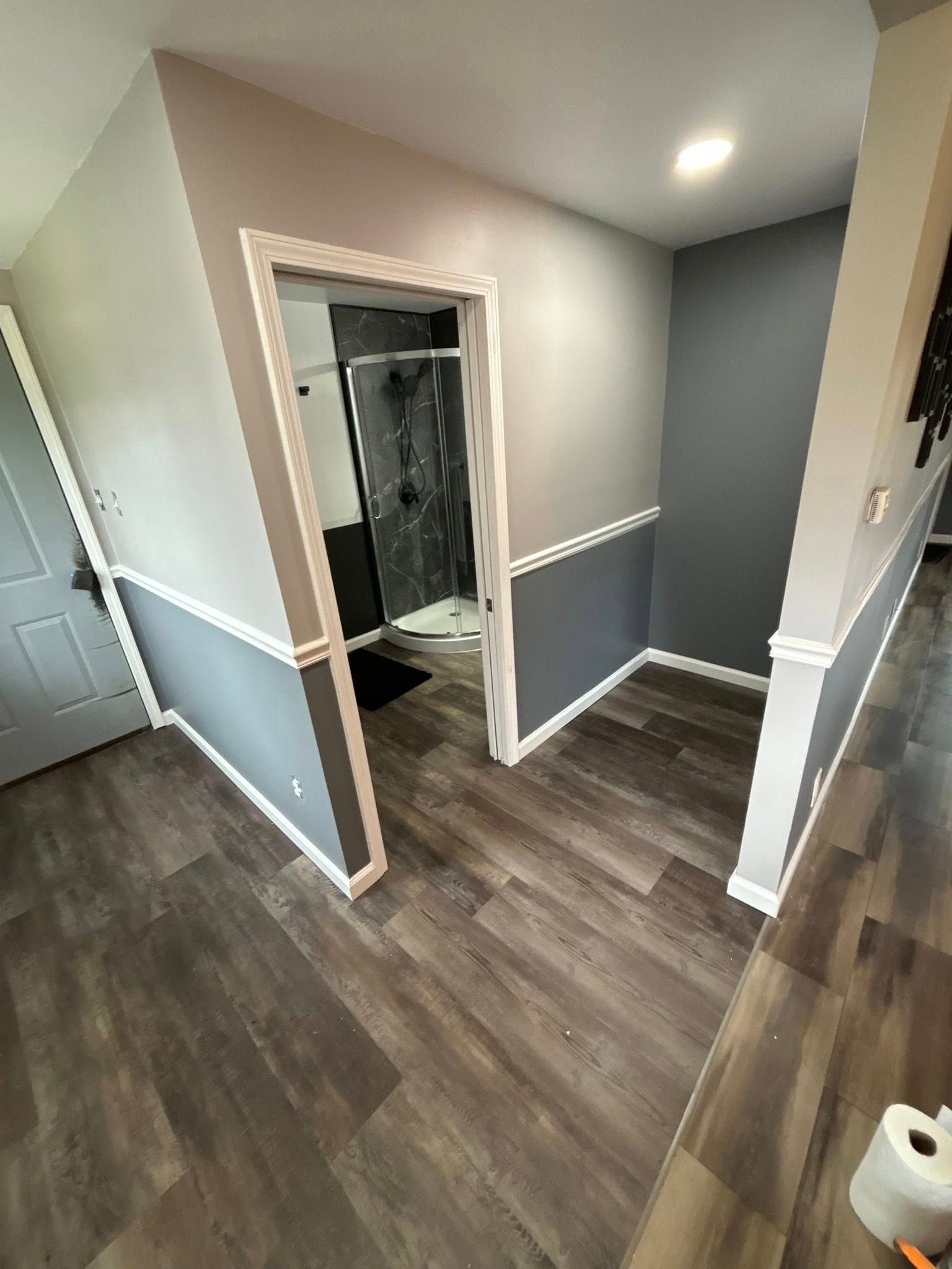 Room with gray and white walls, dark flooring, and a doorway leading to a shower.