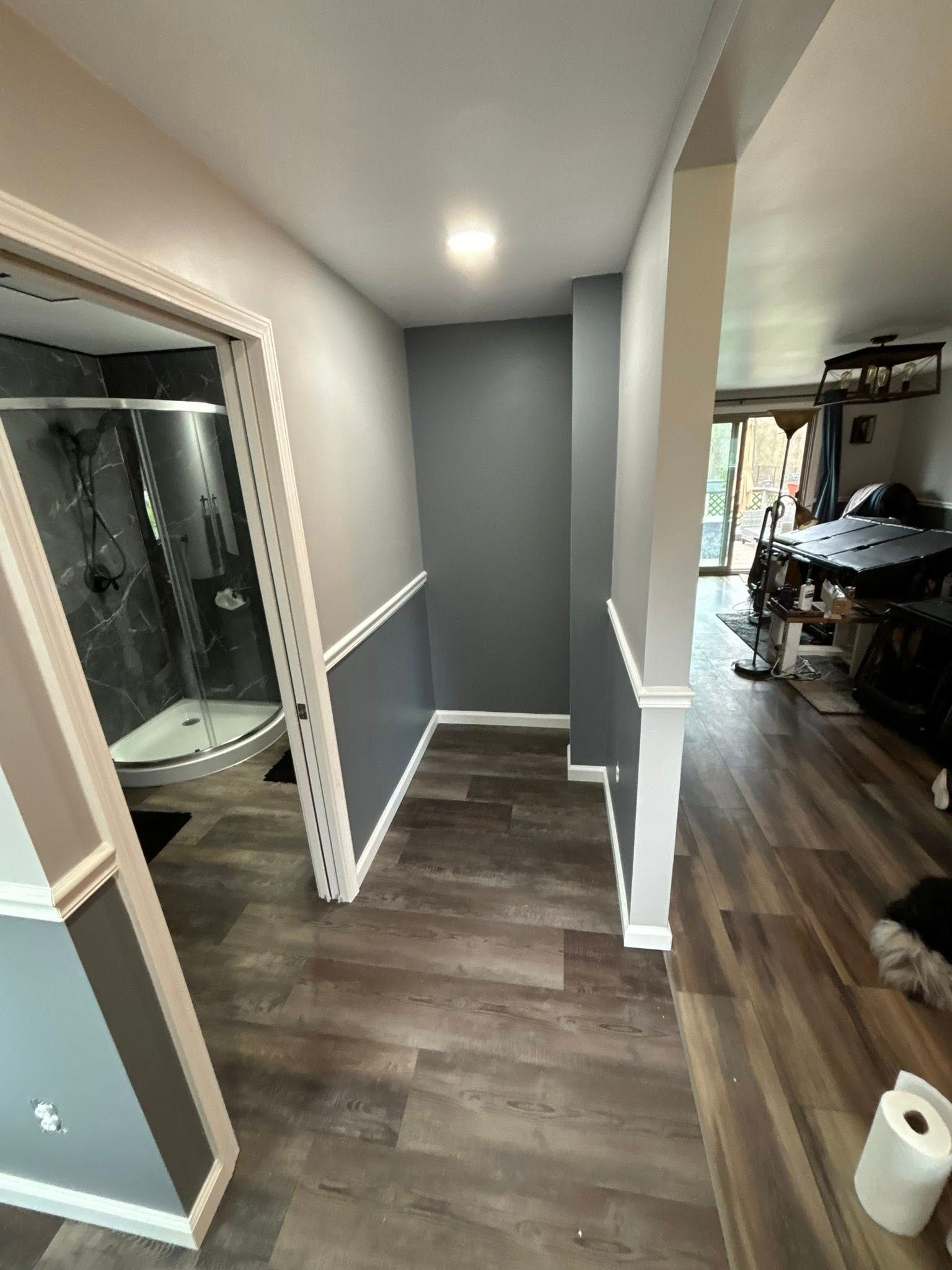Hallway with gray and white walls, wood-look flooring, and a shower visible to the left.
