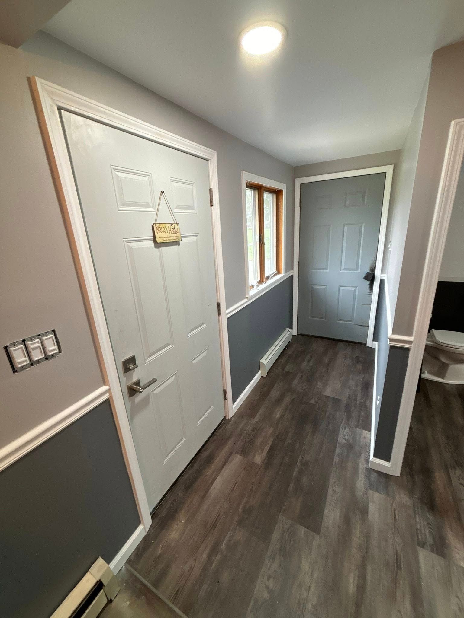 Interior entryway with light gray walls, white trim, and a dark wood-look floor. Two gray doors and a window.