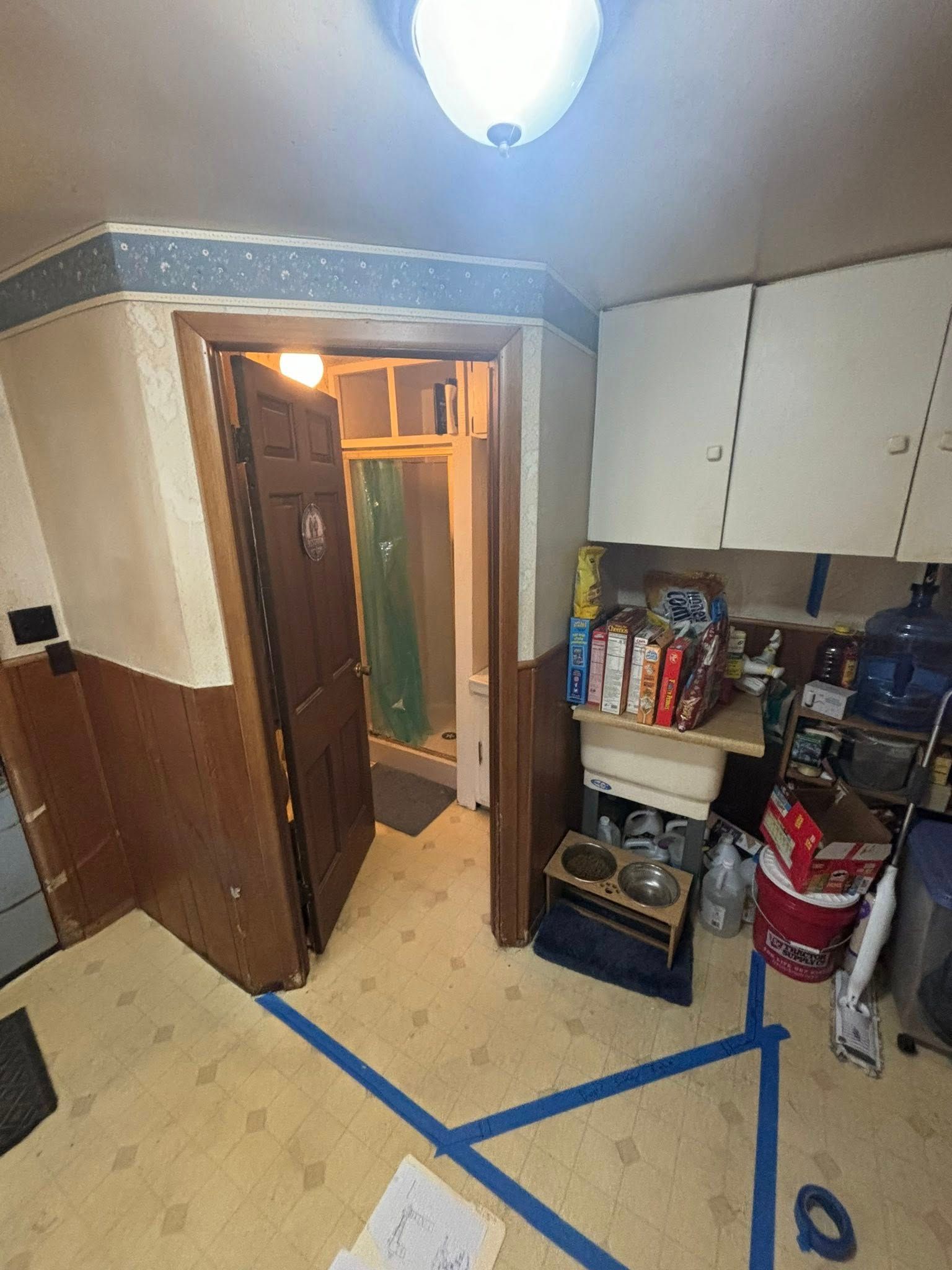 Kitchen with door to bathroom, beige and blue walls, linoleum floor.