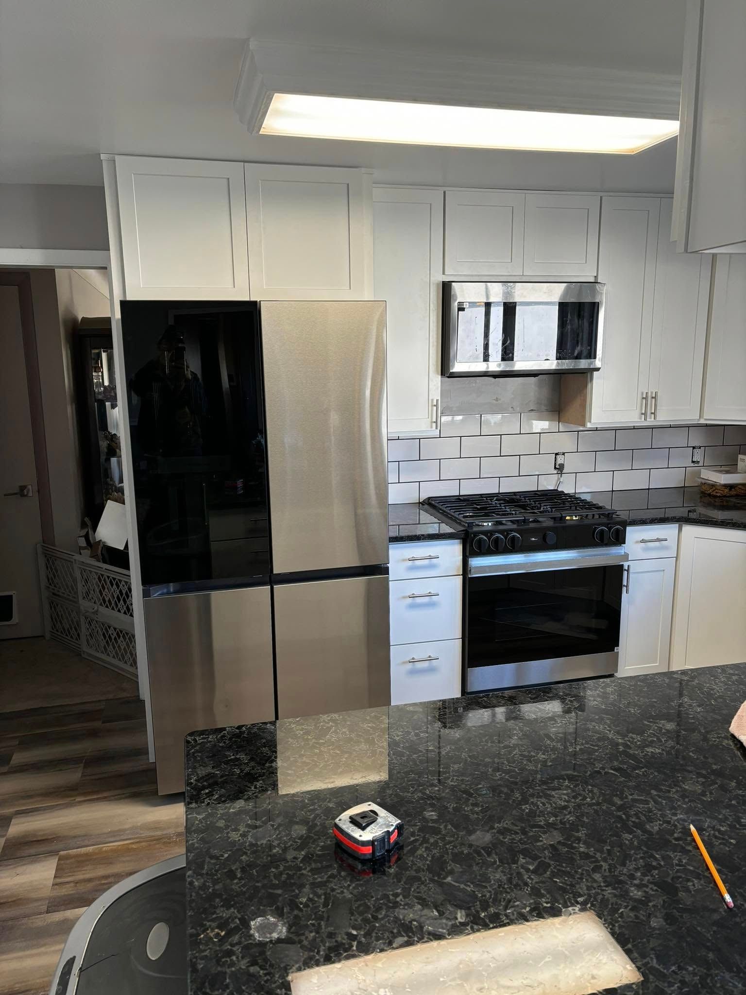 Modern kitchen with stainless steel refrigerator, white cabinets, black countertops, and a gas stove.