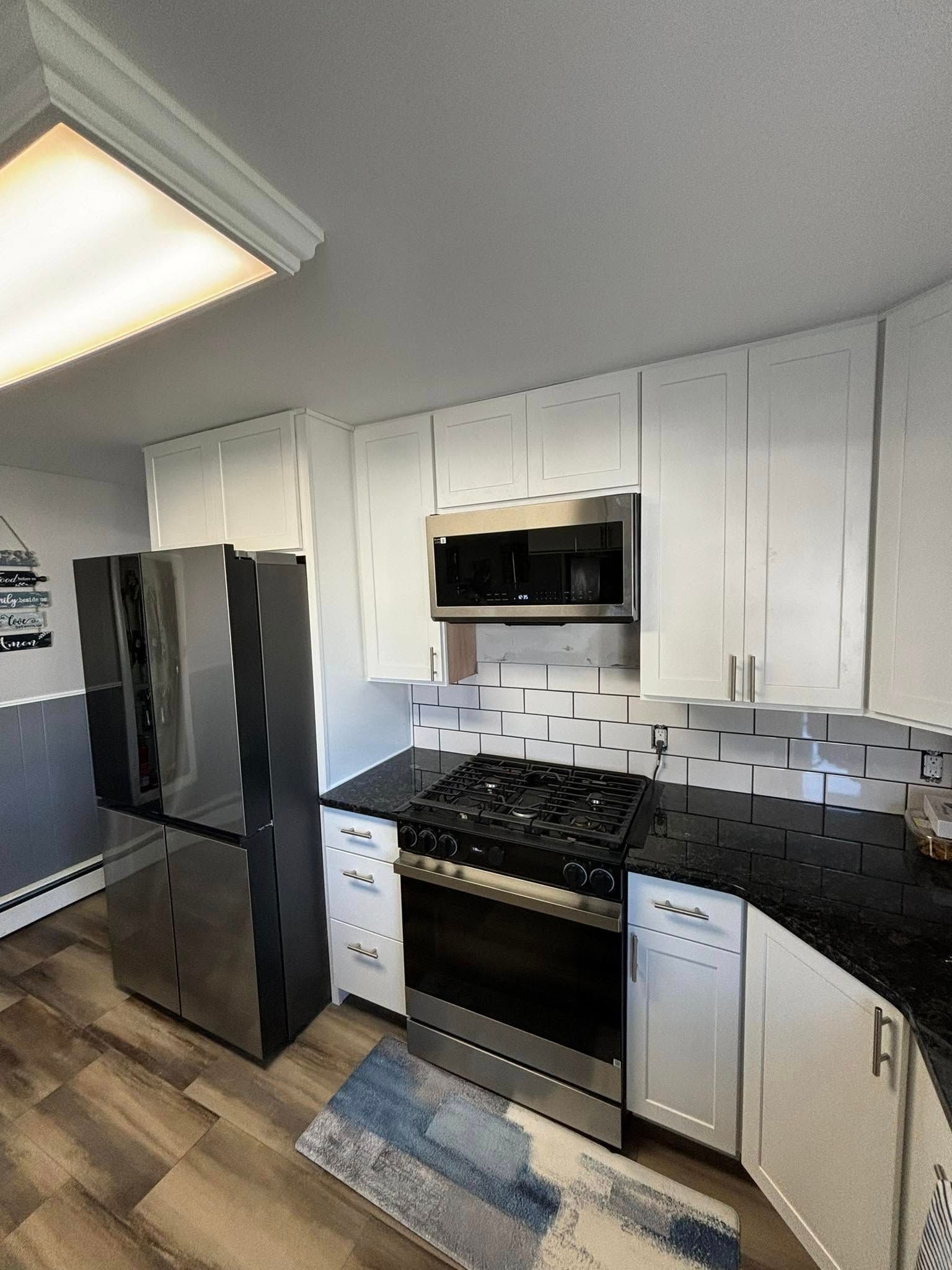 Modern kitchen with white cabinets, stainless steel appliances, and dark countertops.