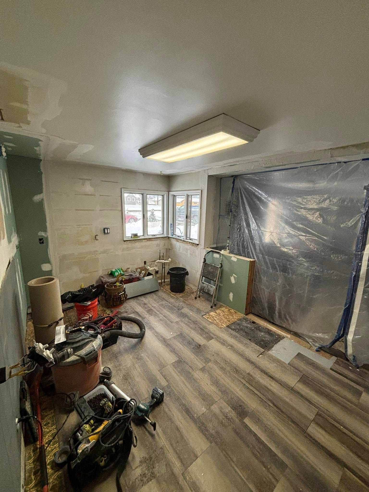 Room under construction with tools, unfinished walls, new flooring, and a window.