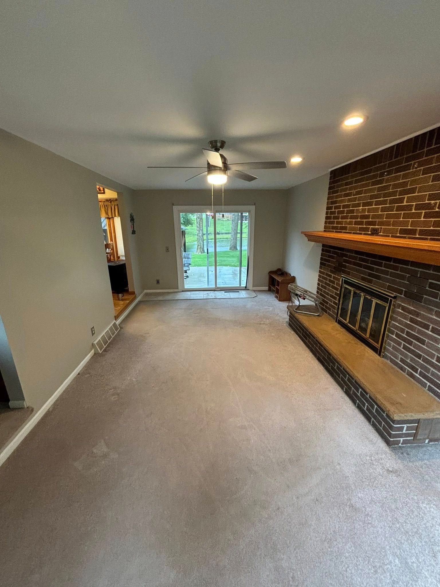 Living room with fireplace, sliding glass door, neutral-colored walls, and gray carpet.