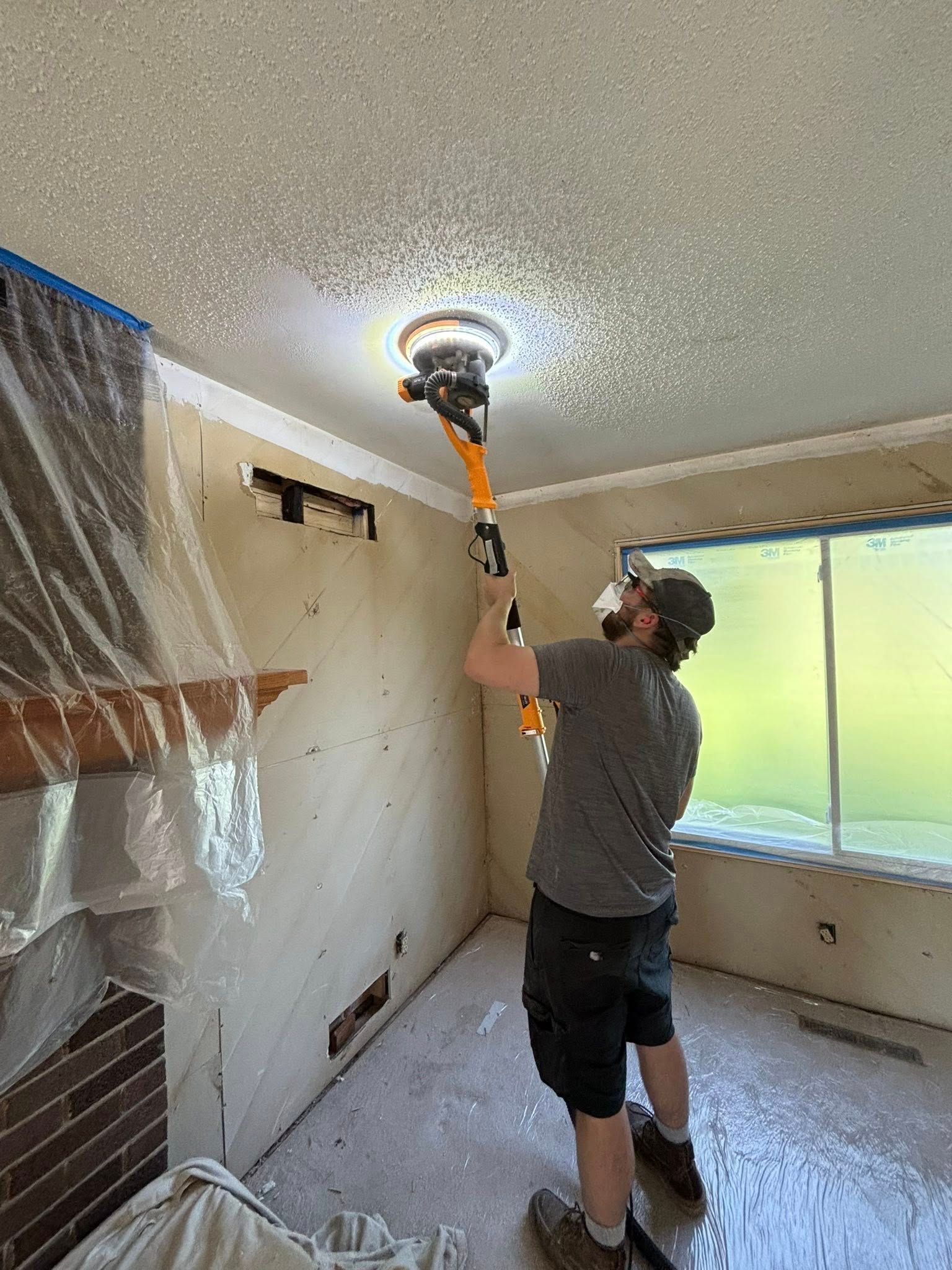 A person sanding a textured ceiling with an extended sander. Interior renovation in progress.