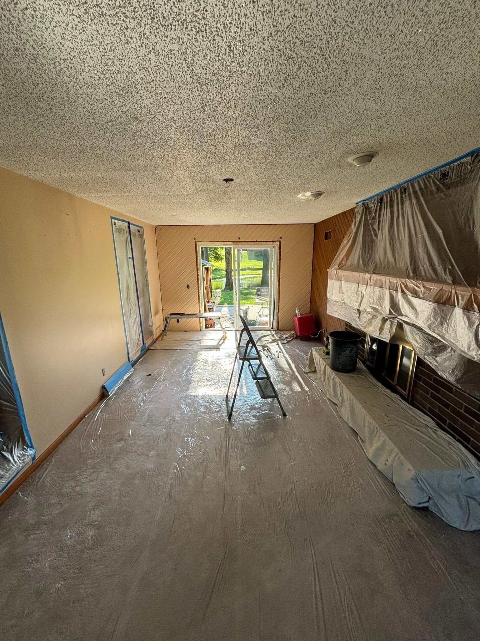 Interior renovation of a room with exposed walls, covered fireplace, and sliding glass door.