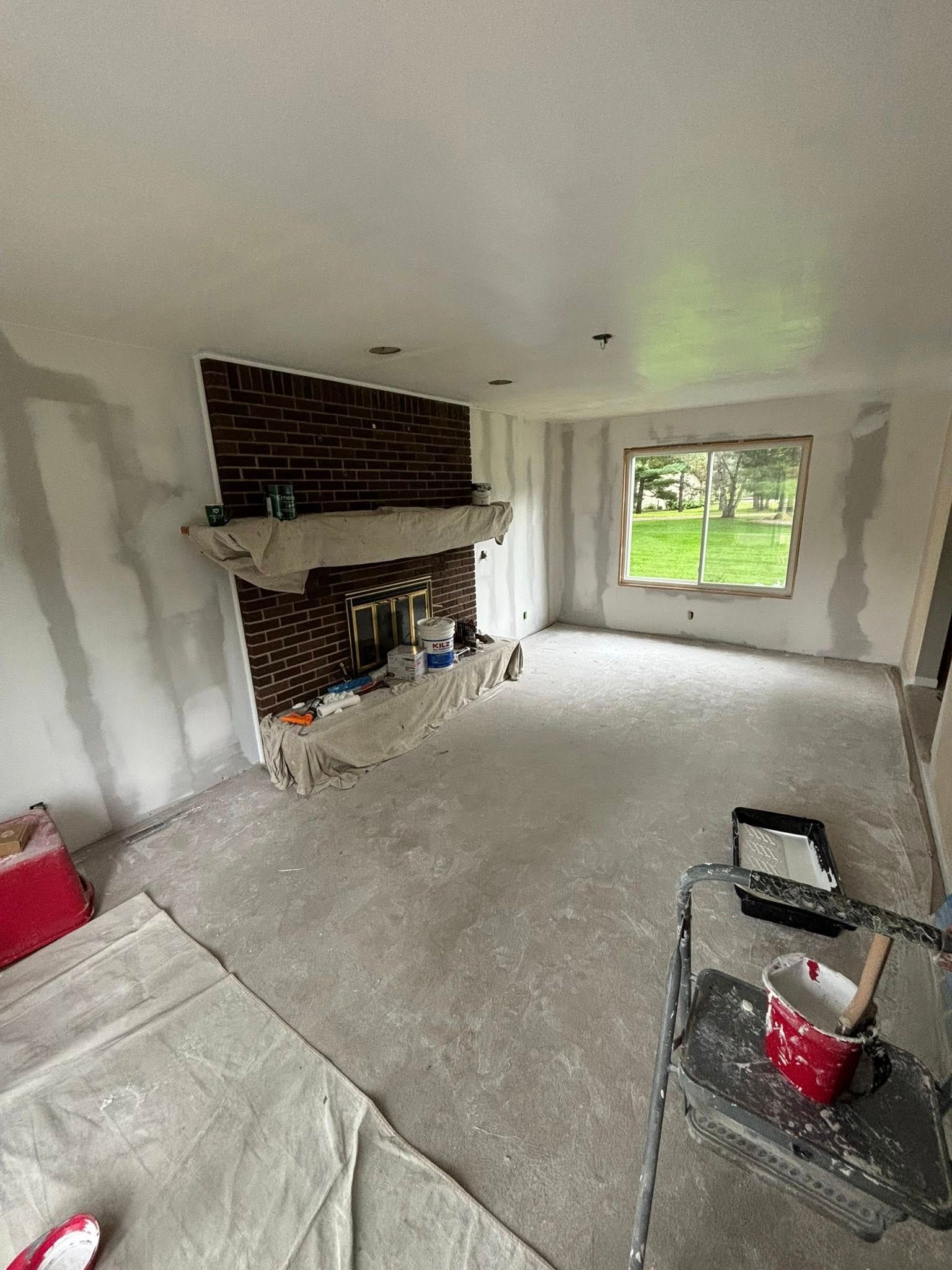 Room with brick fireplace, window, and walls covered in drywall mud, suggesting a renovation project.
