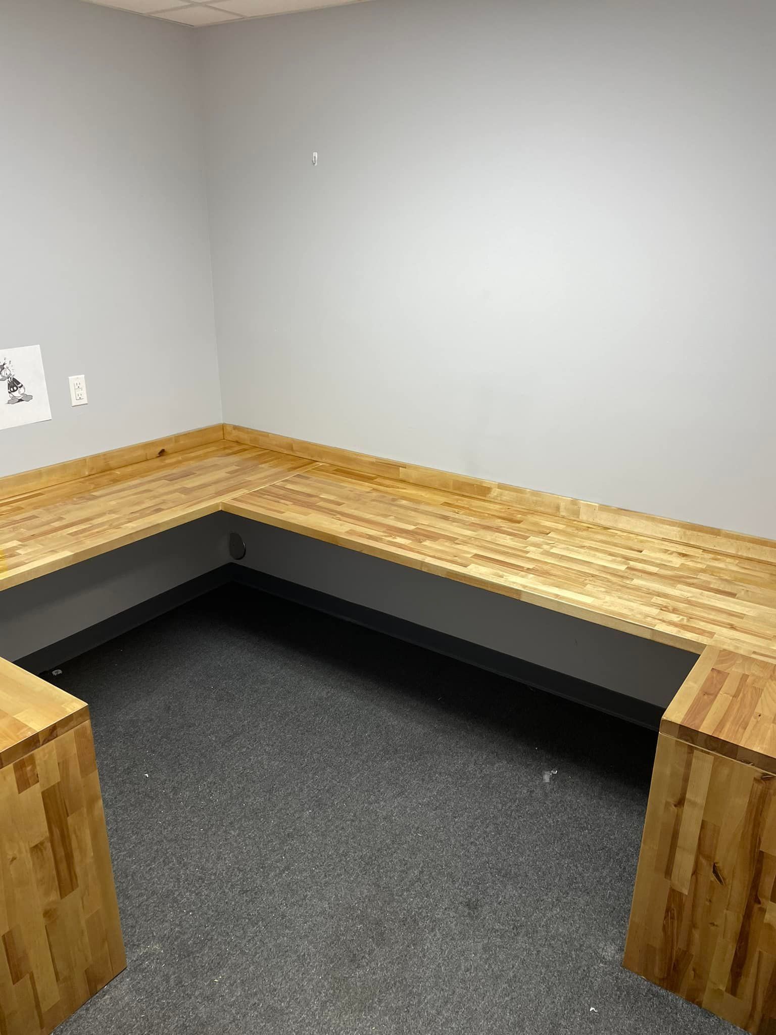 L-shaped wooden bench seat against gray wall, with two wooden cubes on gray carpeted floor in a room.