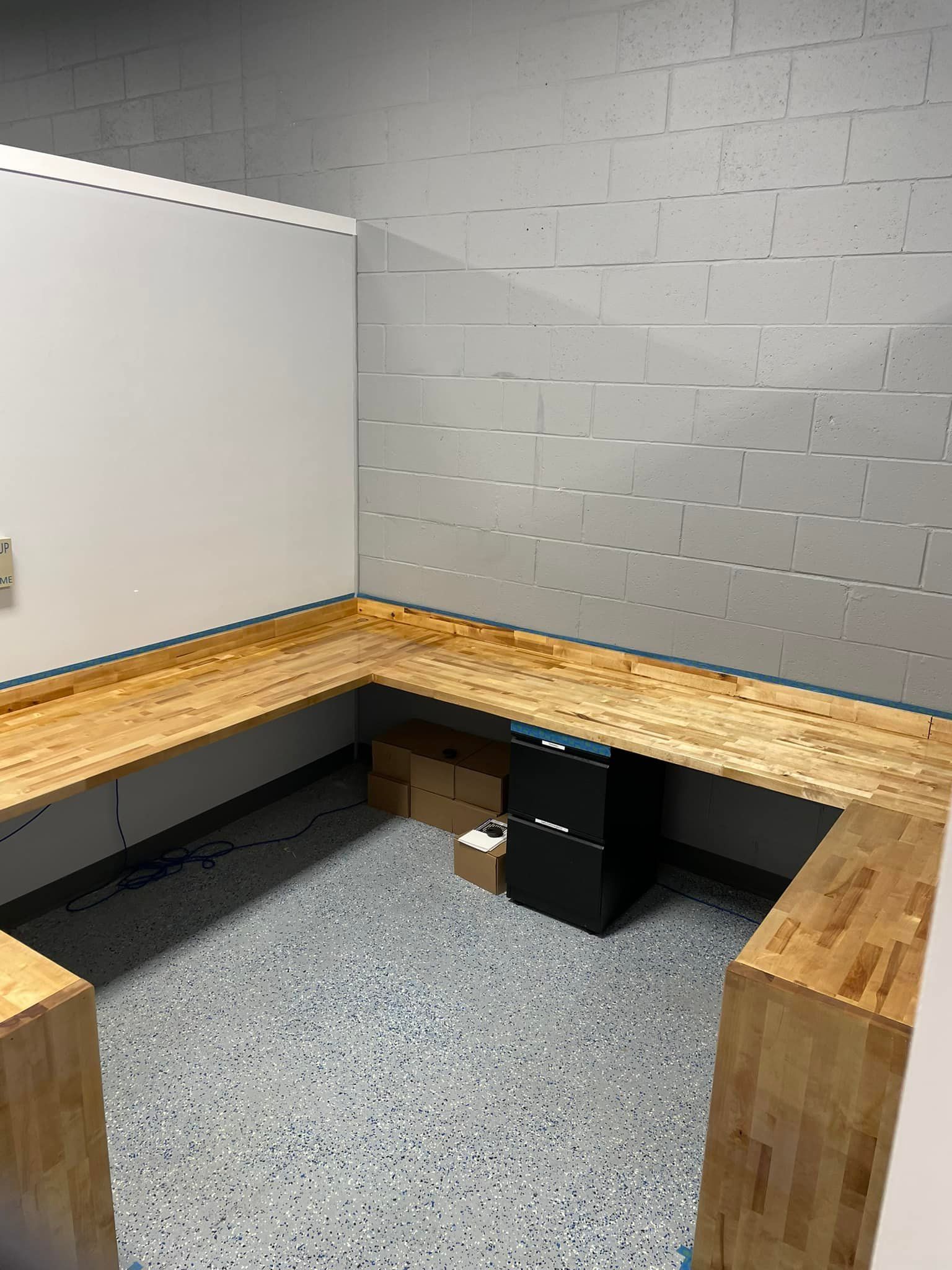 Empty room with a L-shaped wooden bench against gray block and white walls, blue speckled floor.